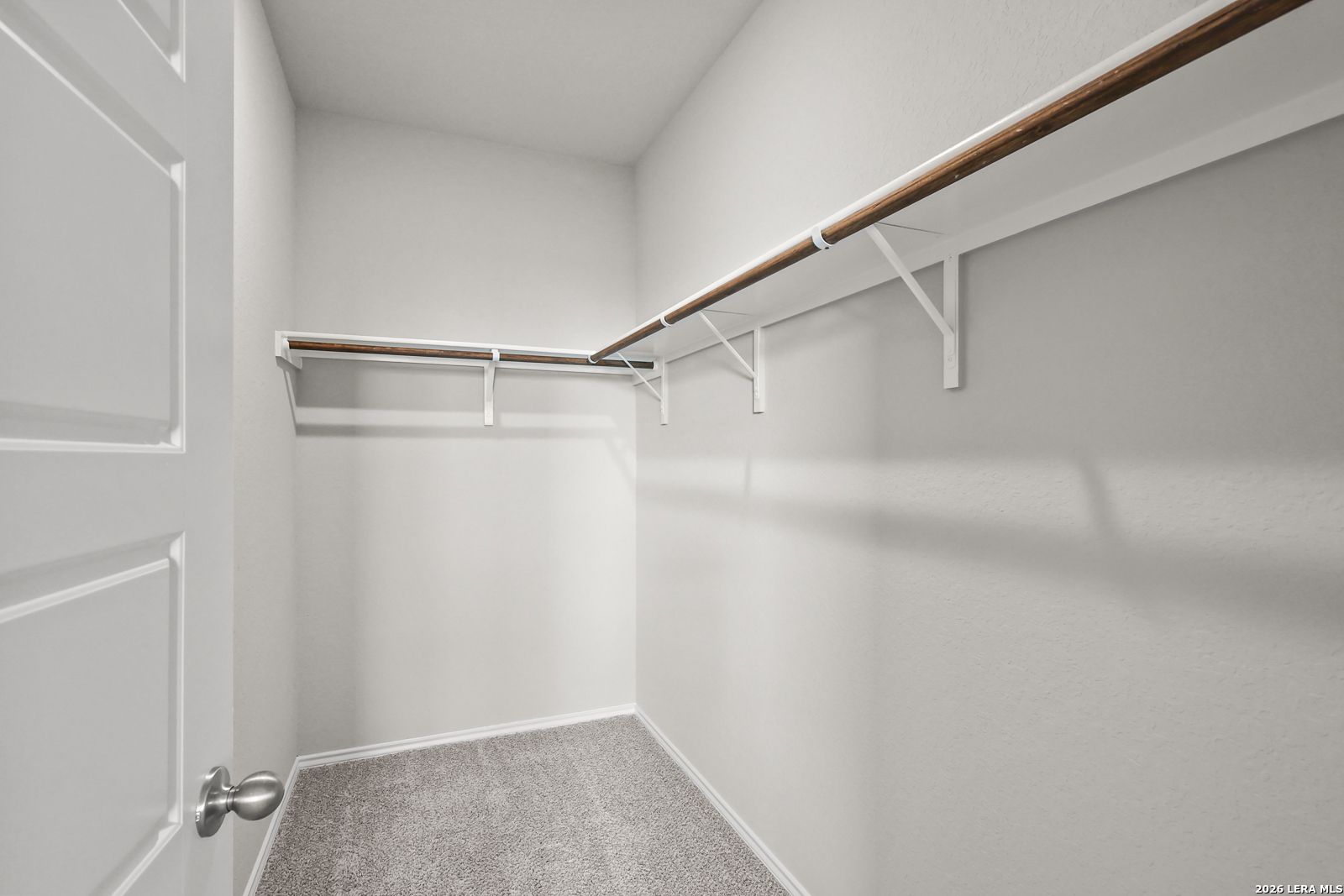 Spacious walk-in closet with wood shelving, hanging rods, white walls, and carpet floor in Davidson Homes The Frio B, San Antonio, Texas