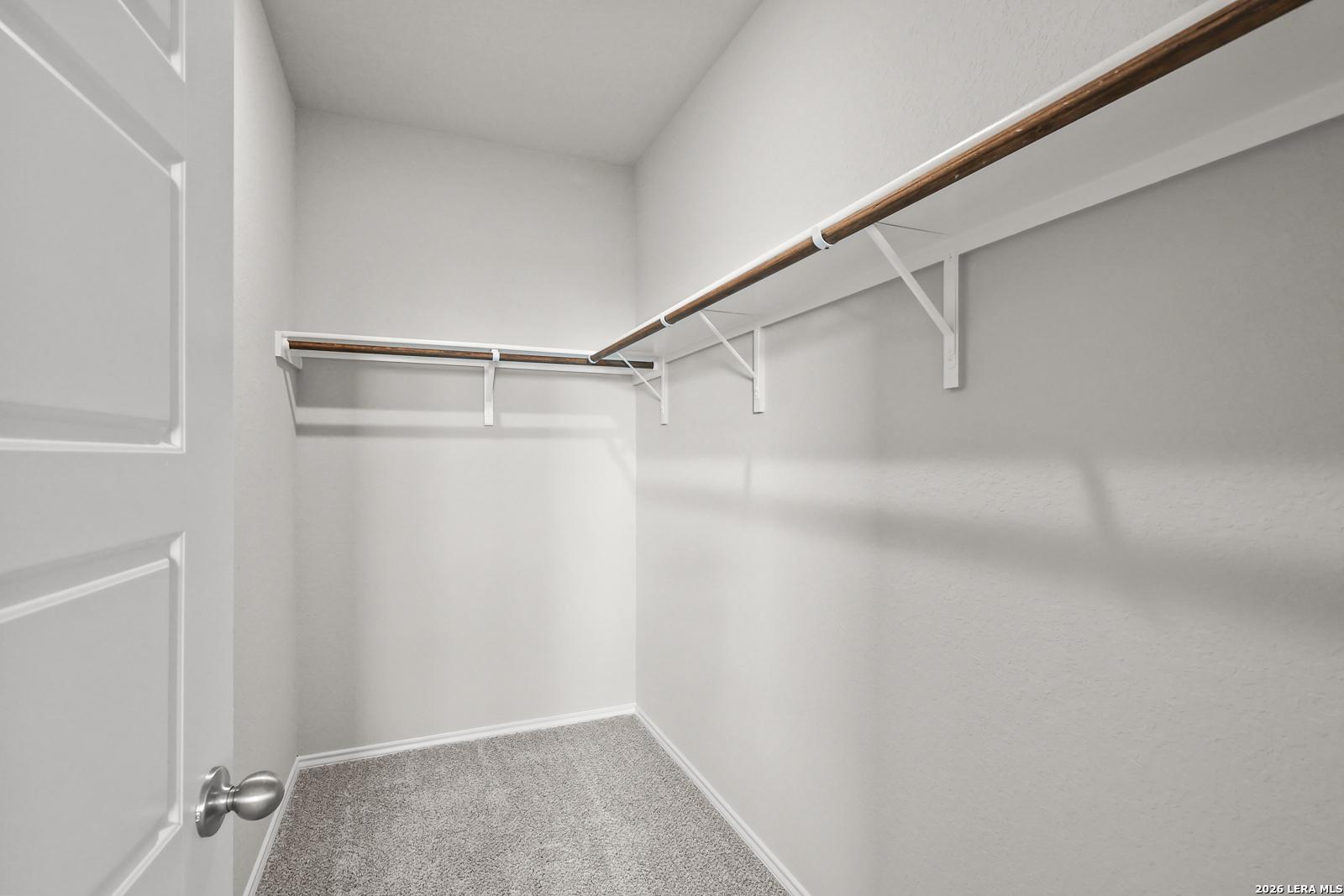 Spacious walk-in closet with wood shelving, hanging rods, white walls, and carpet floor in Davidson Homes The Frio B, San Antonio, Texas