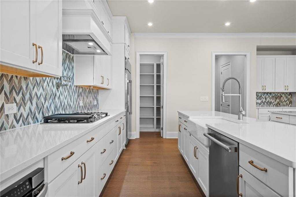 Modern white kitchen with chevron tile backsplash, quartz island, and pantry in Davidson Homes The Arlington A, East Cobb, GA