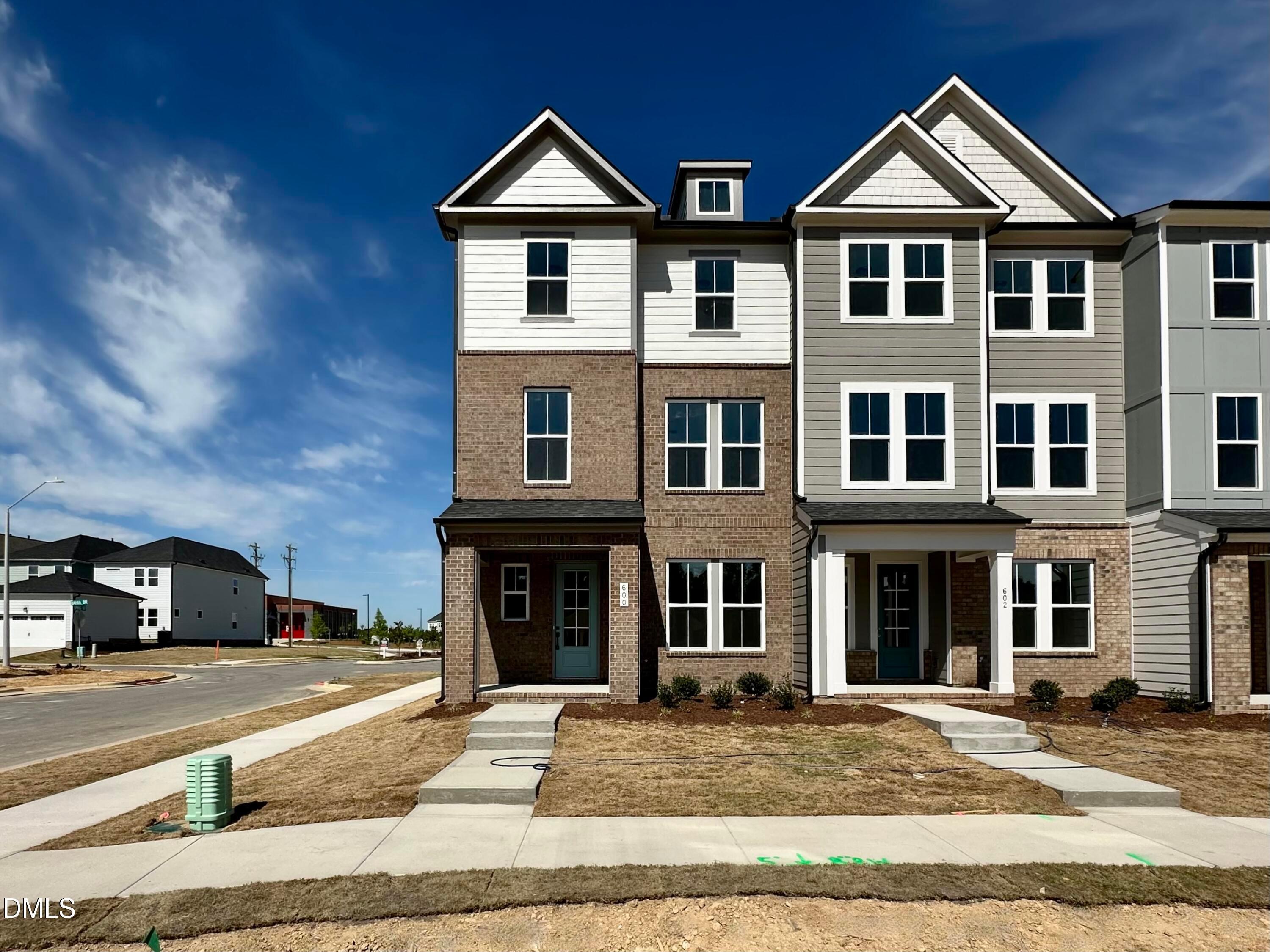 Modern three-story brick townhome with white siding, gabled roof, and blue door in Forestville Yard Townhomes, Knightdale, NC