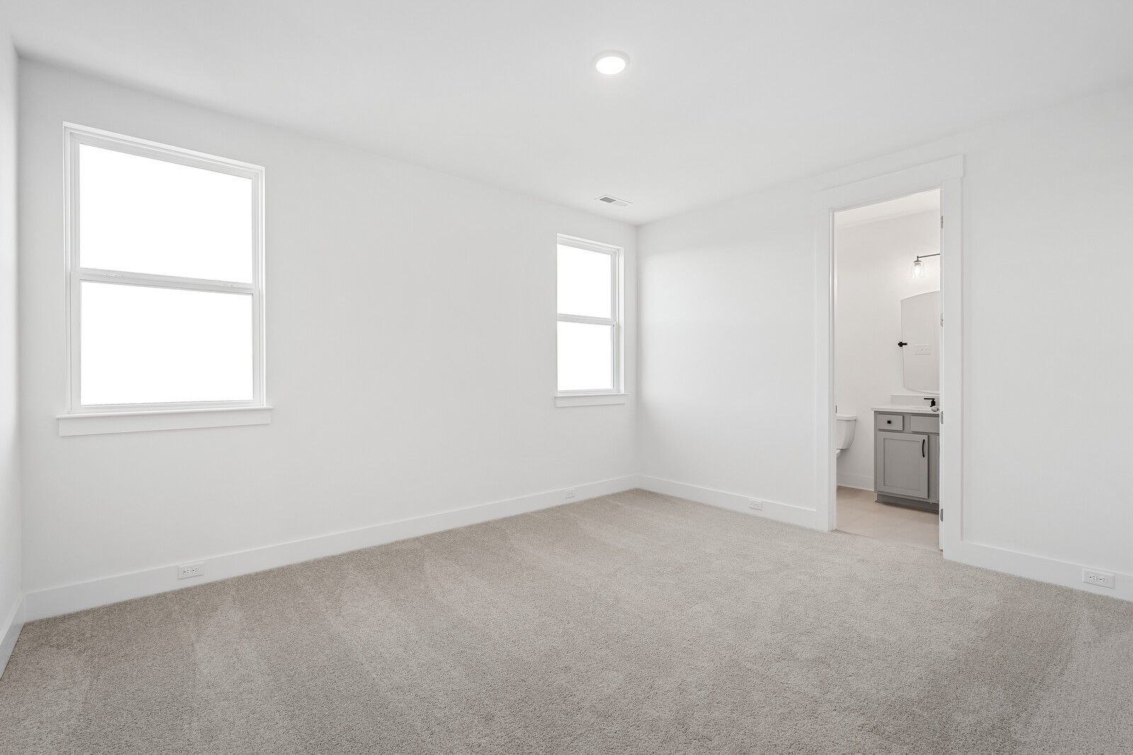 Bright secondary bedroom with white walls, beige carpet, large windows, and adjacent bathroom in Davidson Homes The Alston A, Murfreesboro