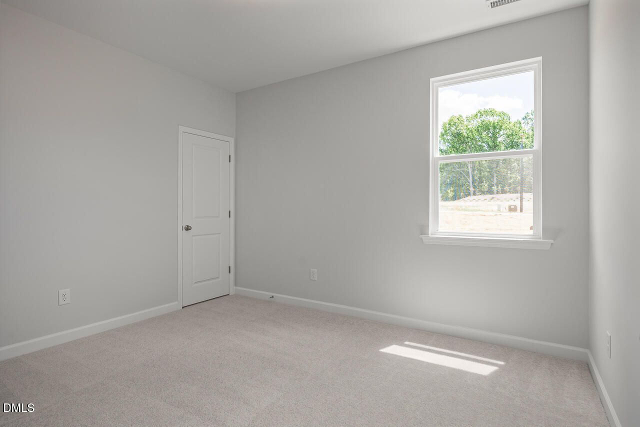 Bright secondary bedroom with neutral carpet and window view in The Birch II E home at Sage on North Main, Wake Forest.