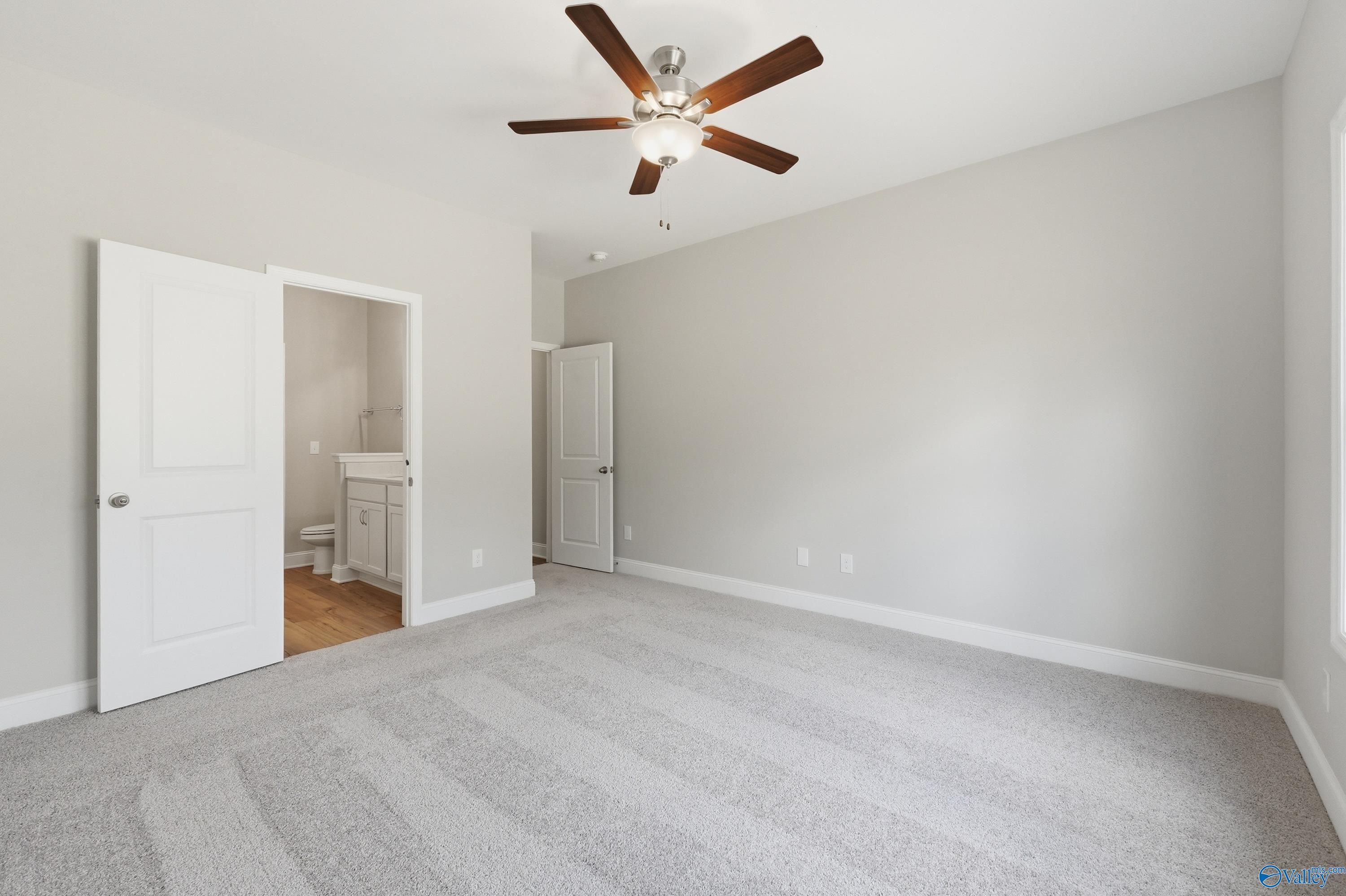 Spacious gray-carpeted bedroom with ceiling fan and en-suite bathroom in Davidson Homes The Asheville, Huntsville AL