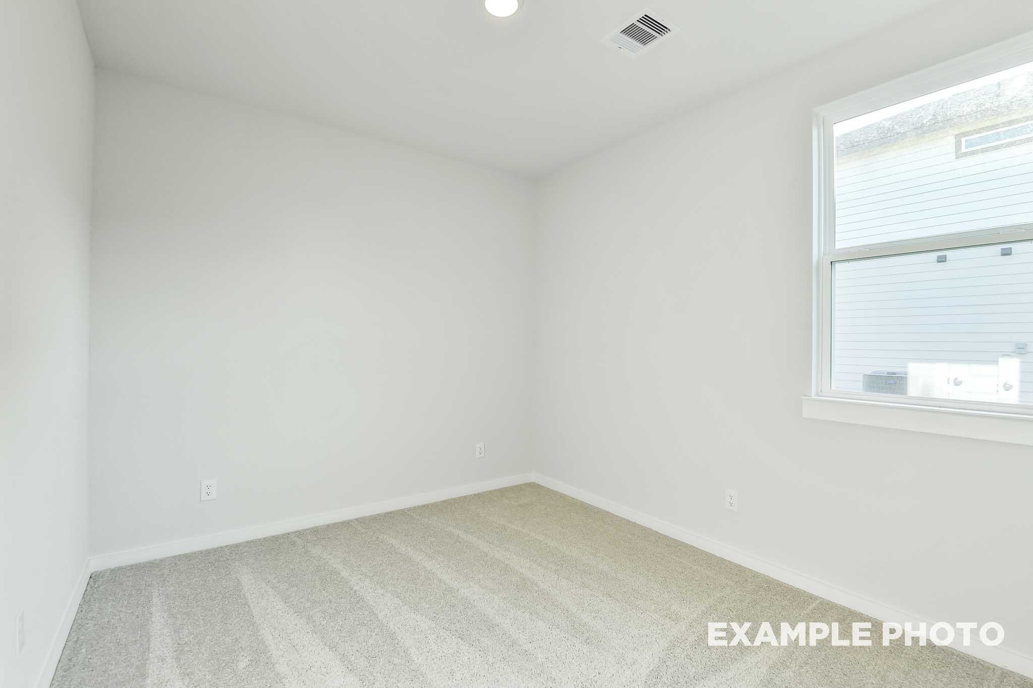 Bright empty bedroom with white walls, carpet flooring, and large window in The Colorado by Davidson Homes, Beasley, TX