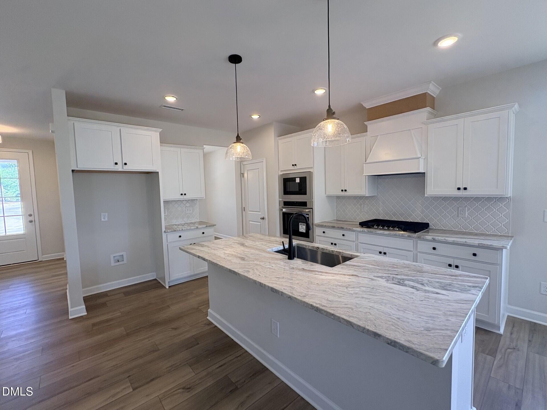 Modern kitchen with white cabinets, stone countertops, and kitchen island in The Ash C floor plan, Woodland Crossing, Zebulon.