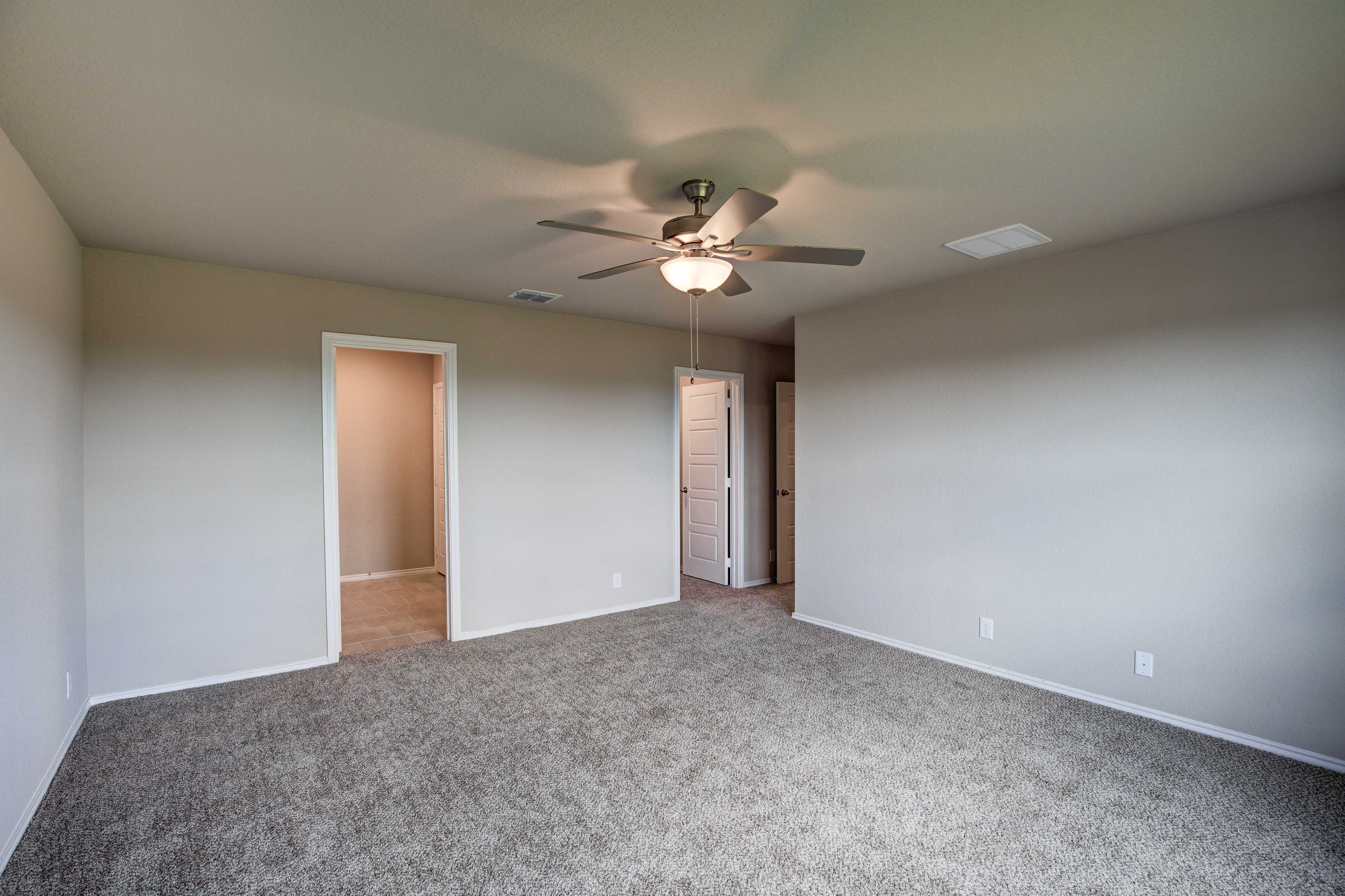 Spacious master bedroom in The Murray home with neutral walls, carpet floor, ceiling fan, and doors to bath and closet