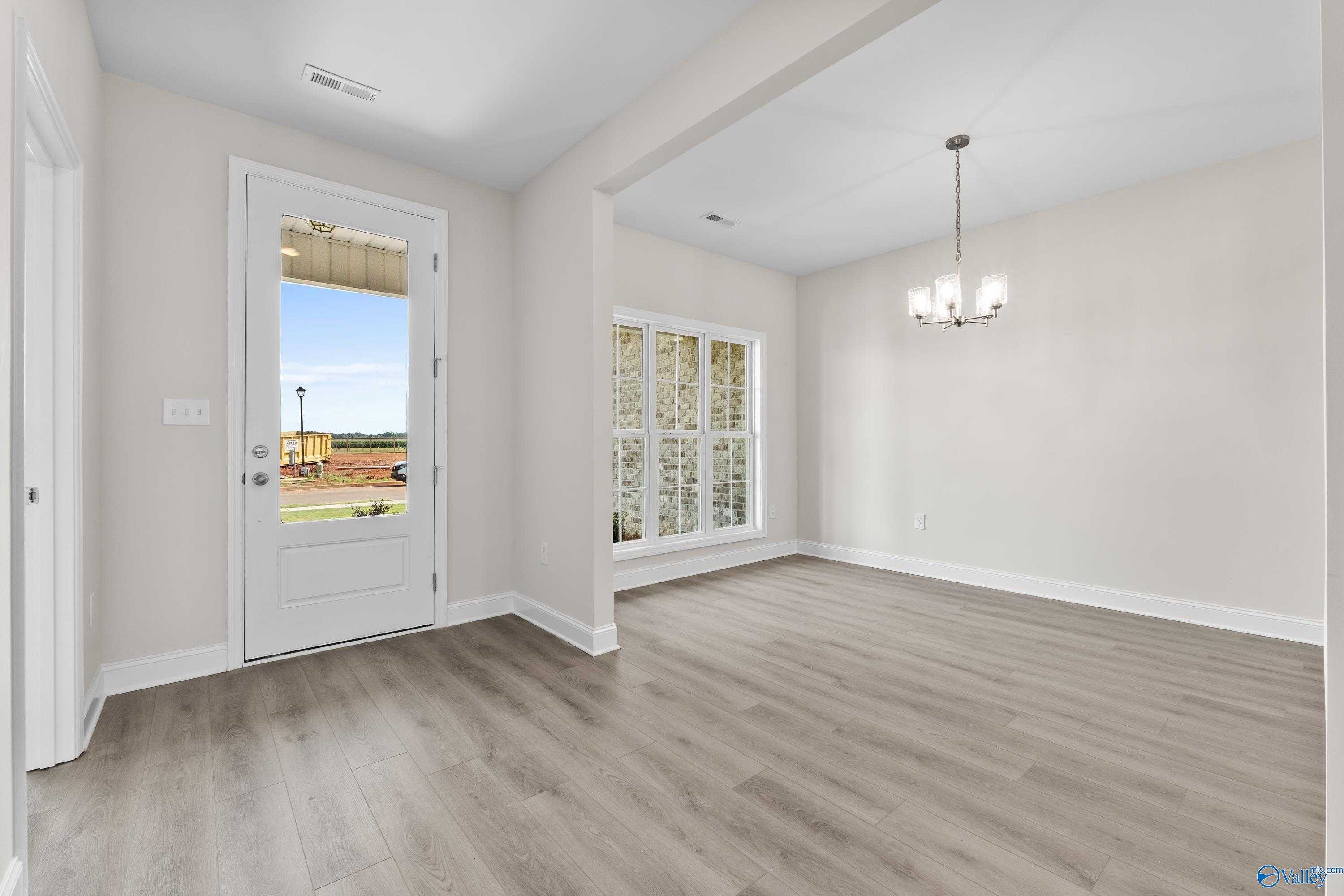 Bright entryway with light wood floors, chandelier, and backyard view through glass door in Davidson Homes Finleigh, Toney, Alabama