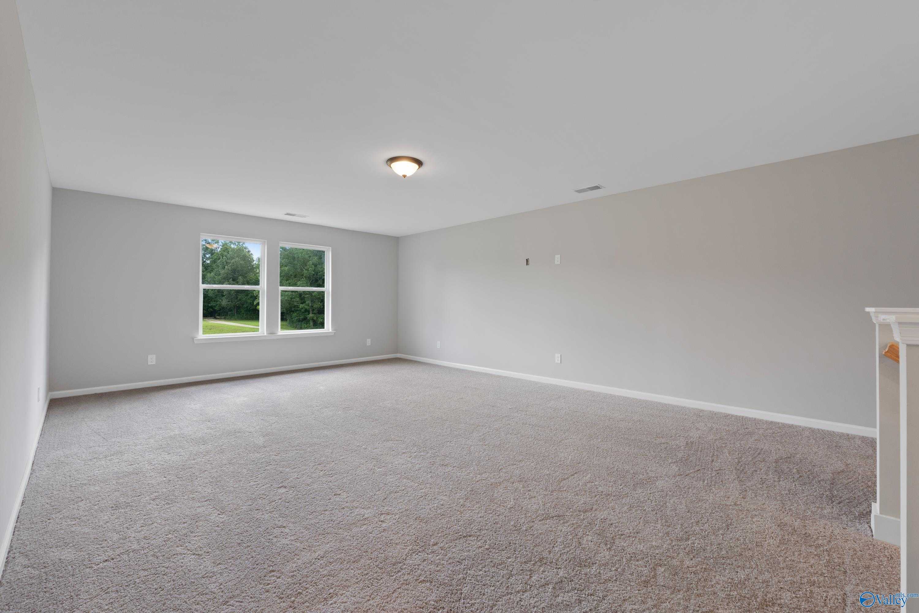 Spacious empty bedroom with gray walls, beige carpet, large windows, and fireplace mantel in Davidson Homes The Dorado, Huntsville