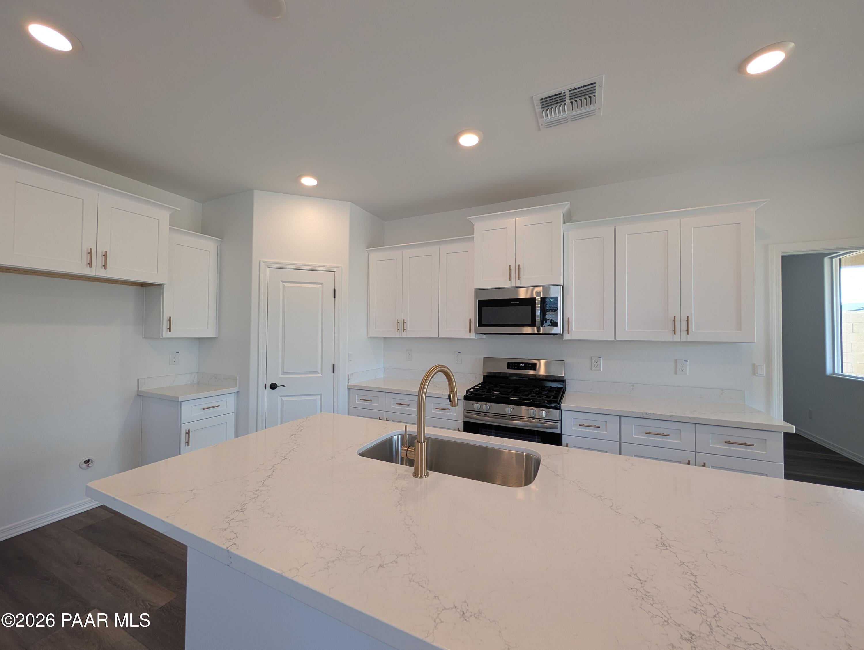Modern kitchen with white cabinets, quartz countertops, and island in The Malibu B floor plan, South Ranch, Prescott.