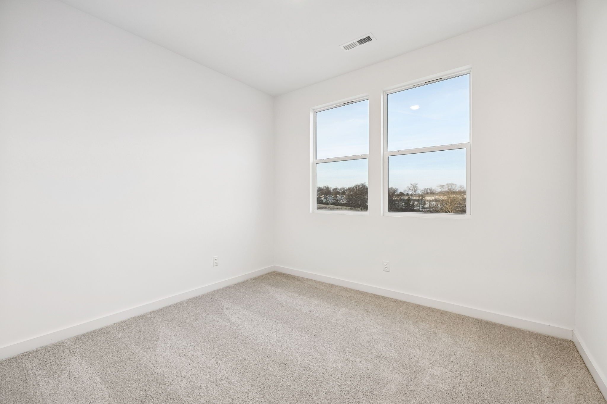 Bright empty bedroom with large double windows overlooking trees, beige carpet, white walls in The Willow, Davidson Homes, White House, TN