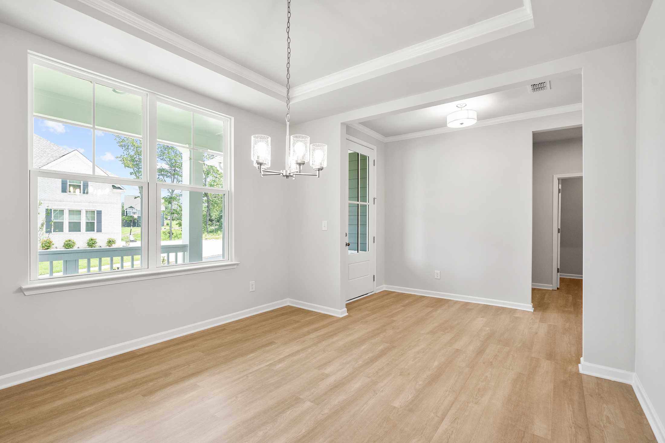 Spacious dining room in The Ash B home with light hardwood floors, chandelier, large windows, and French doors in Hoschton GA