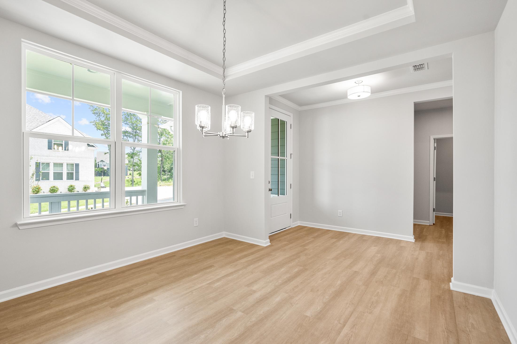 Spacious dining room in The Ash B home with light hardwood floors, chandelier, large windows, and French doors in Hoschton GA