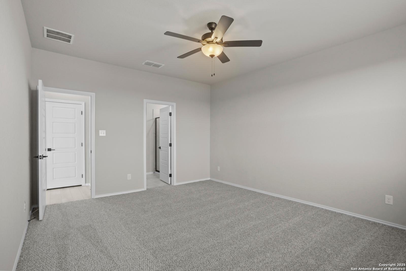 Spacious empty bedroom with gray carpet, neutral walls, ceiling fan, and adjacent doors in The Daphne H, Seguin, Texas