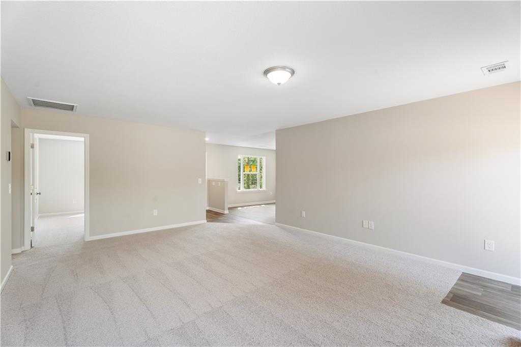 Spacious open living area with beige walls, carpet flooring, and large window in Evermore Homes The Washington, Phenix City, Alabama