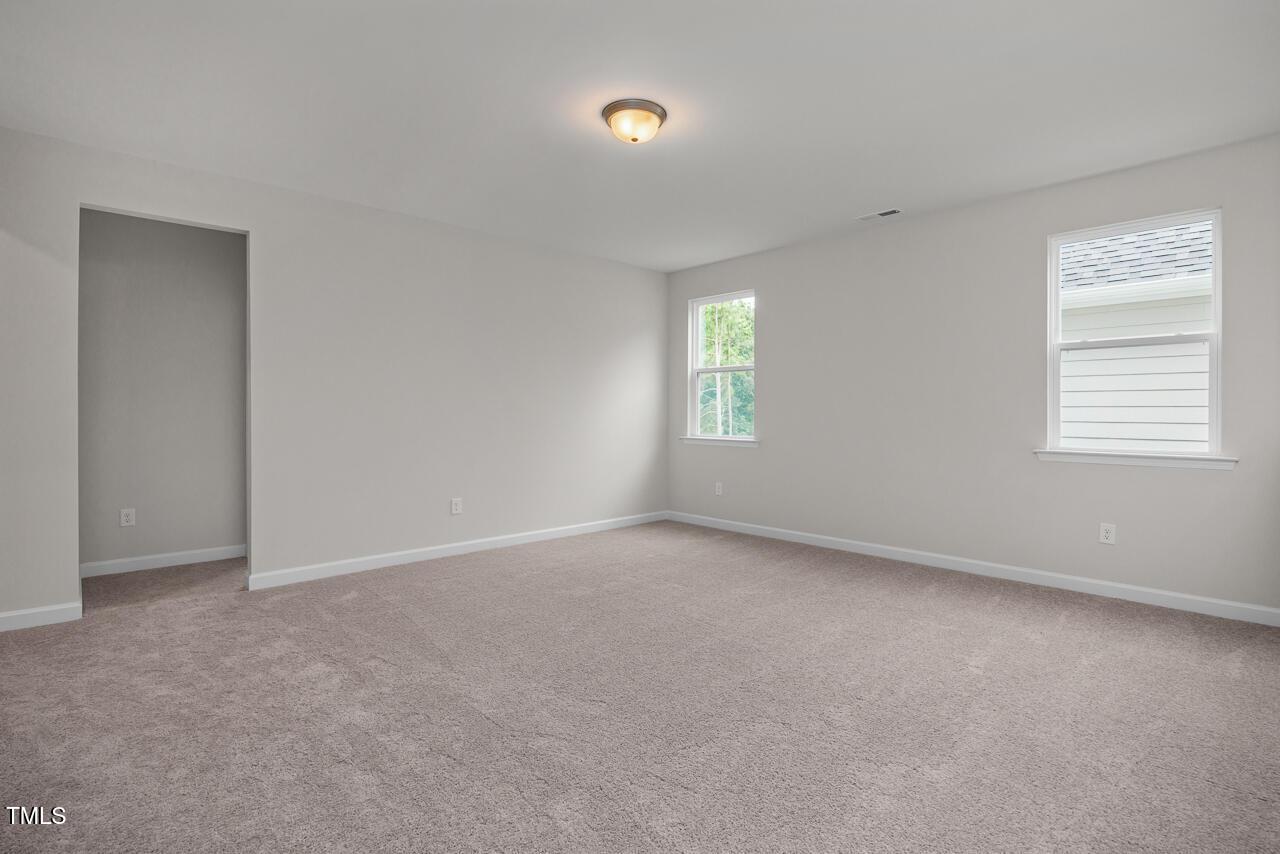 Bright empty bedroom with neutral gray walls, beige carpet, large windows, and open doorway in Davidson Homes The Aspen B, Wake Forest, NC