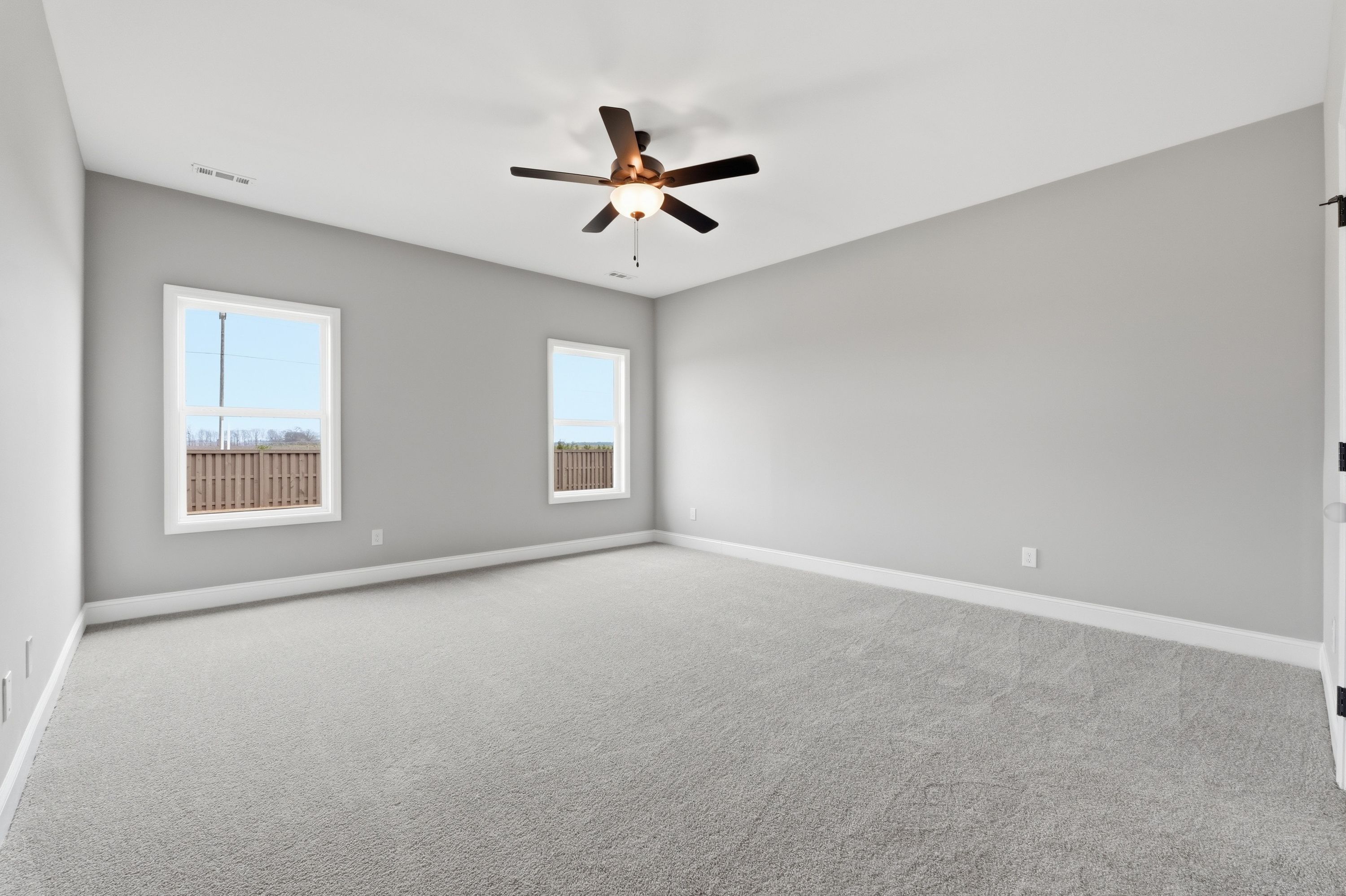 Spacious master bedroom in The Rockford by Davidson Homes with gray walls, carpet floor, ceiling fan, and large windows