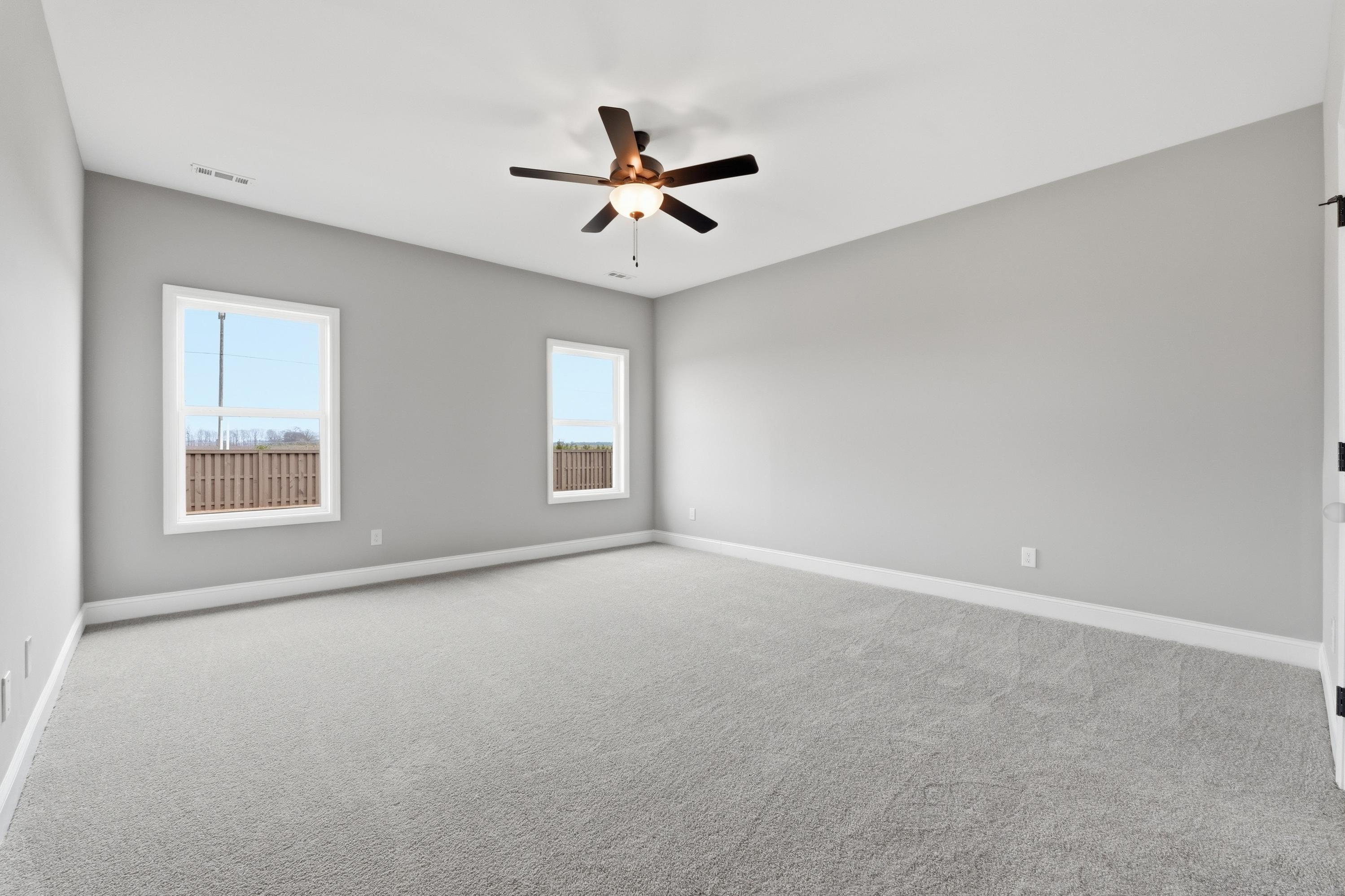 Spacious master bedroom in The Rockford by Davidson Homes with gray walls, carpet floor, ceiling fan, and large windows
