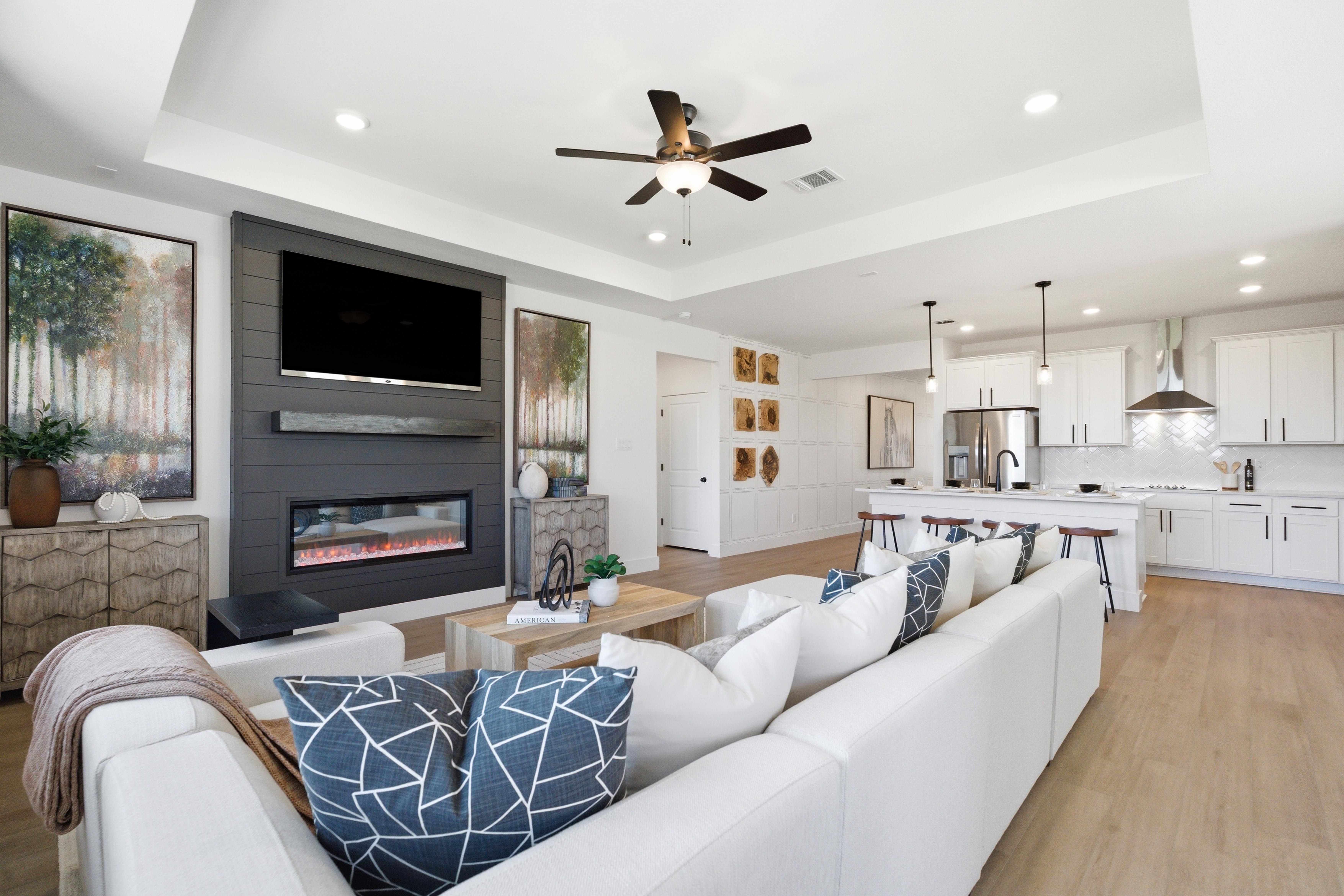 Open-concept living room and kitchen at Mercer Meadows in Royse City Texas with white sofa modern fireplace hardwood floors and white cabinets