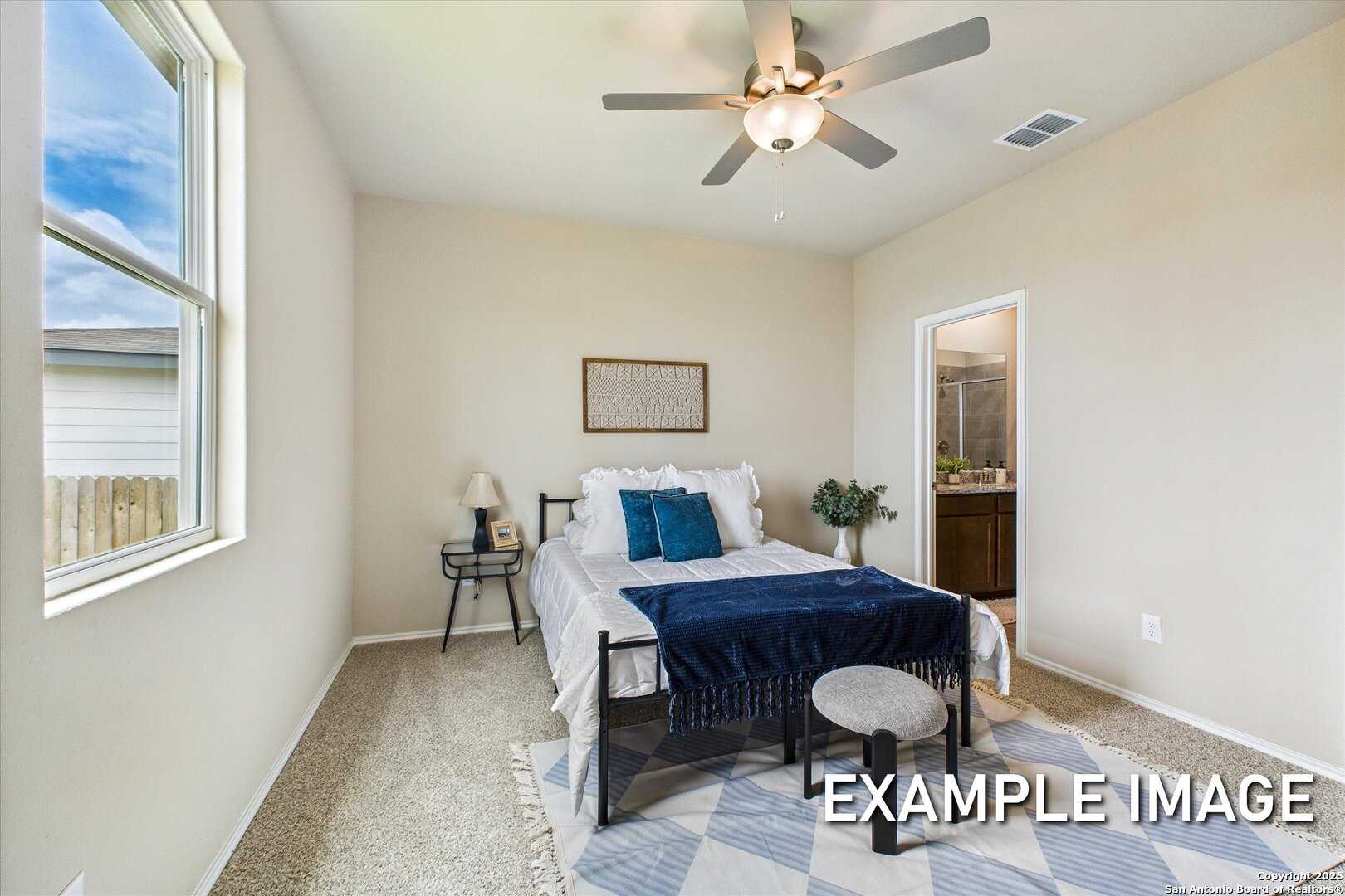 Sunlit secondary bedroom with ceiling fan, metal queen bed, blue bedding, and en-suite bath in Davidson Homes The Comal B, San Antonio
