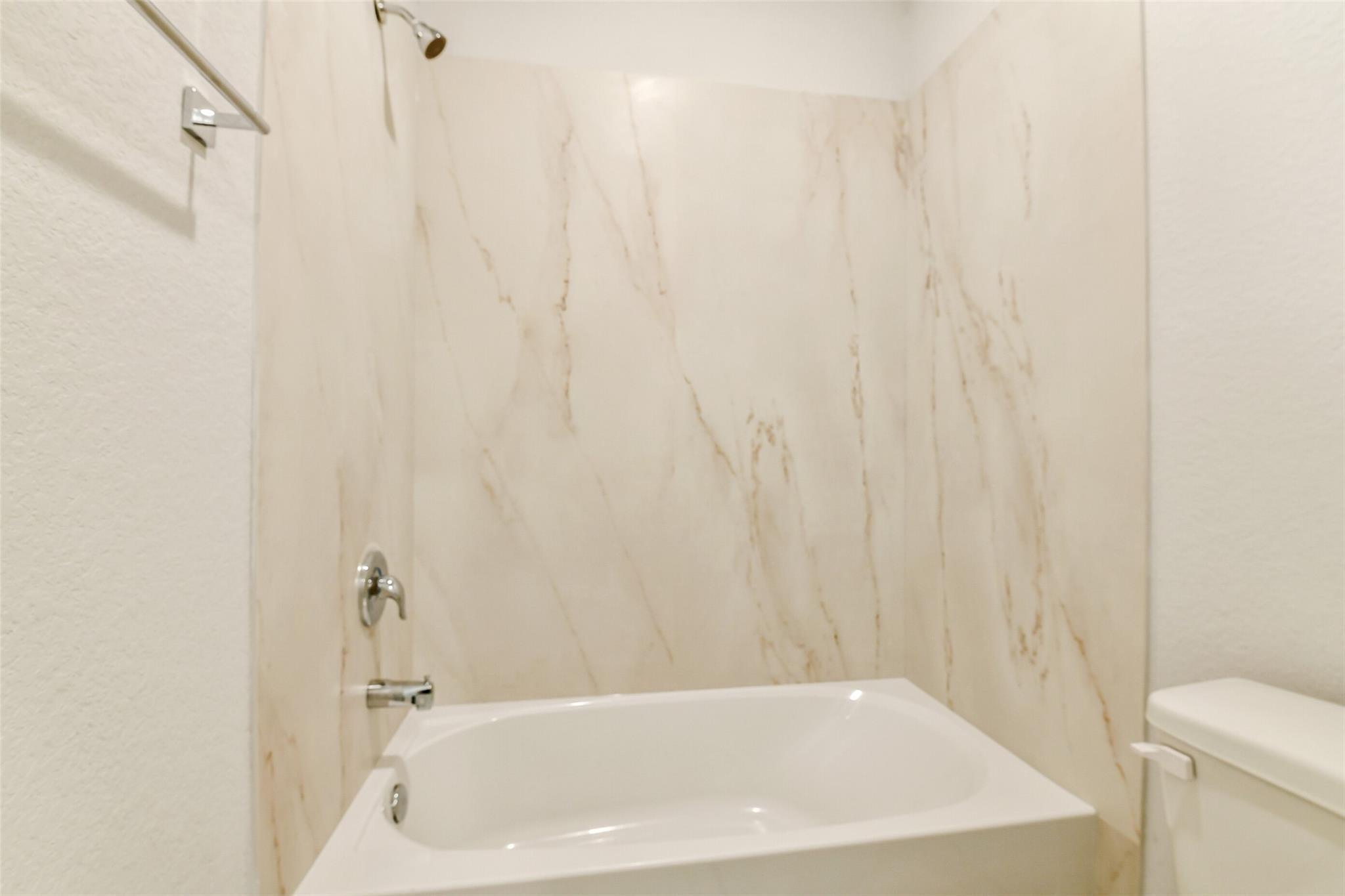 Modern bathroom with marble-look tiled walls, soaking tub, shower, and toilet in Davidson Homes The Colorado F, Cleveland, Texas