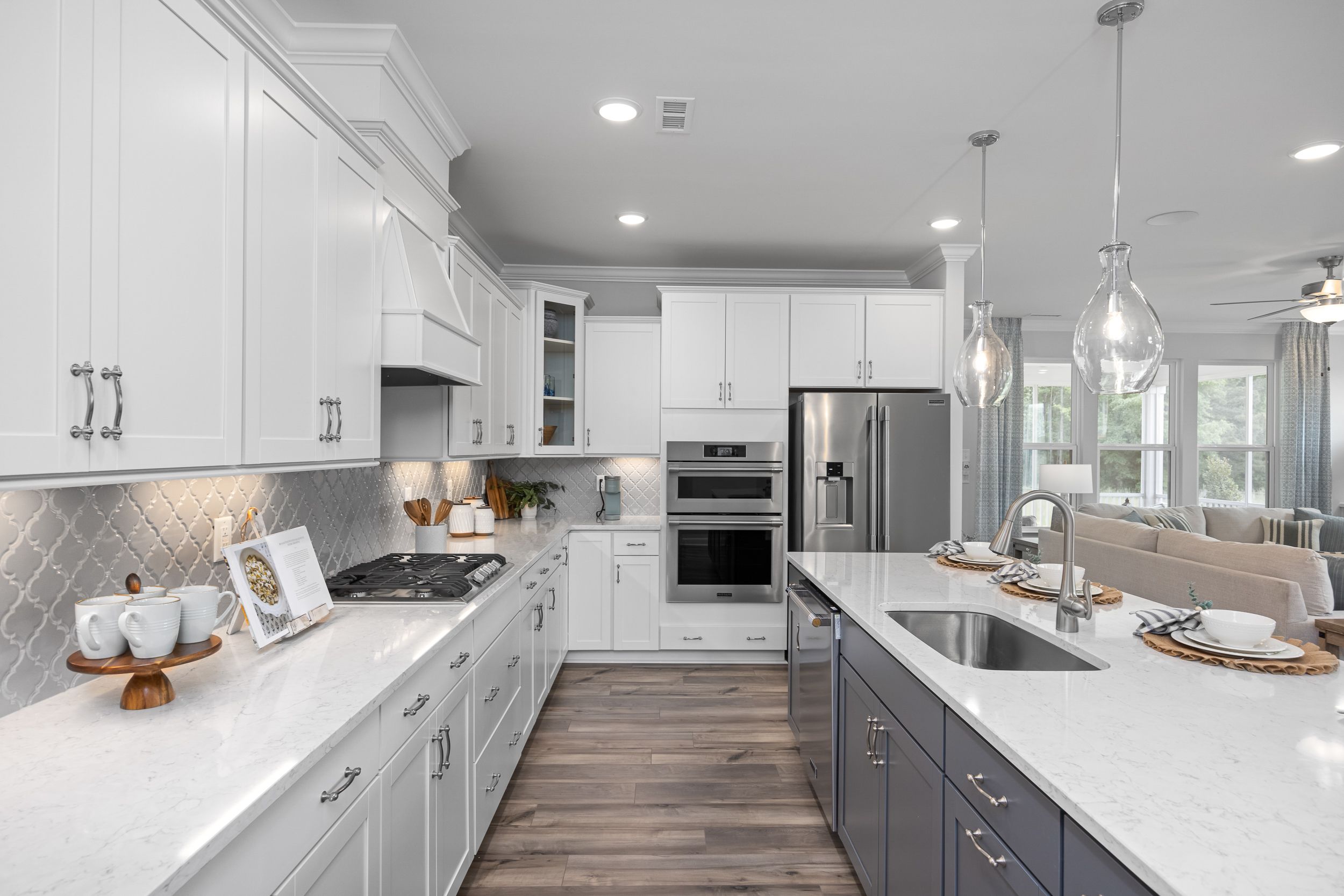 Spacious modern kitchen in Addison West, Holly Springs NC featuring white shaker cabinets, navy island, quartz counters and hardwood floors
