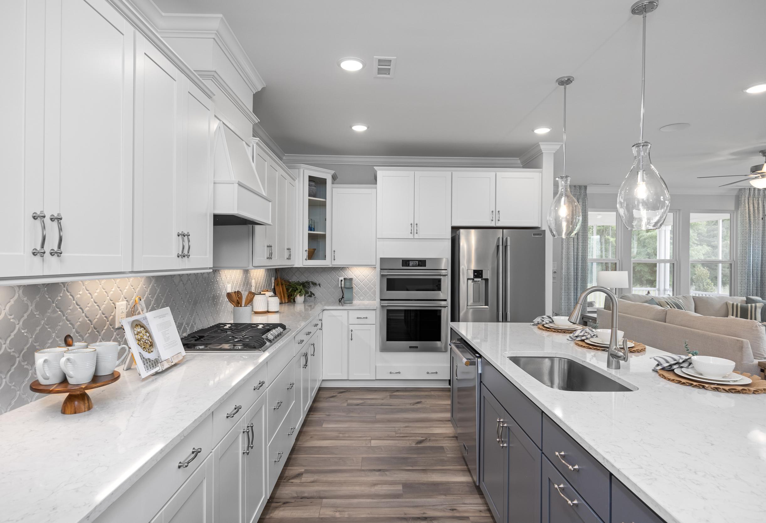 Spacious Magnolia A kitchen with white shaker cabinets, navy island, quartz counters, stainless appliances, and open living area