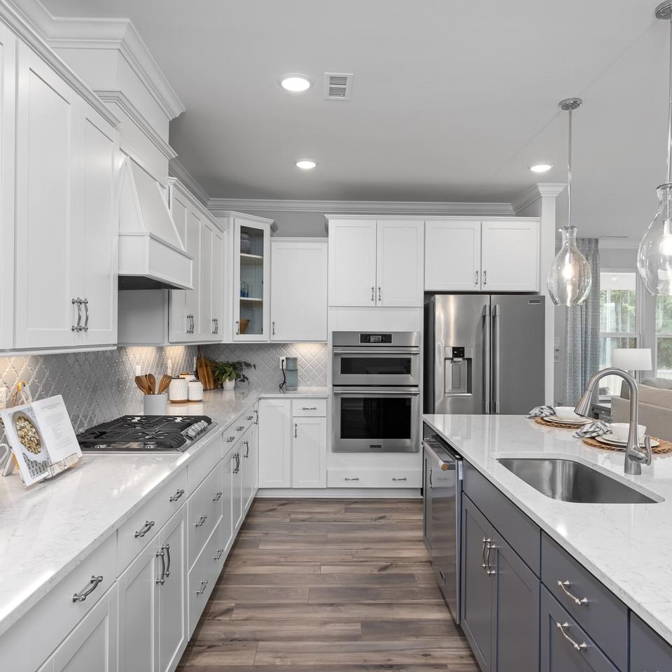 Modern kitchen with white cabinets, quartz countertops, and stainless steel appliances at Springvale South in Fuquay-Varina.