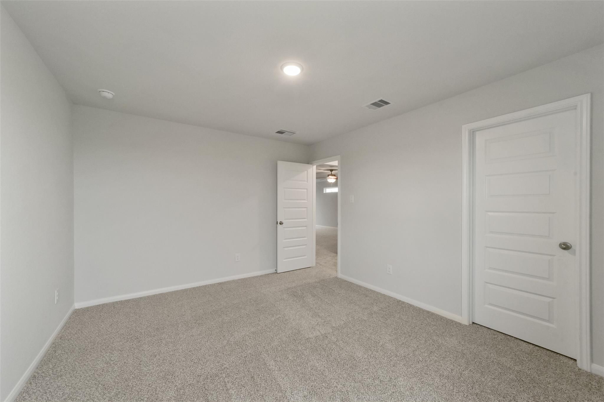 Spacious empty bedroom with neutral gray walls, beige carpet, and double doors in Davidson Homes The San Marcos E, Beasley, Texas