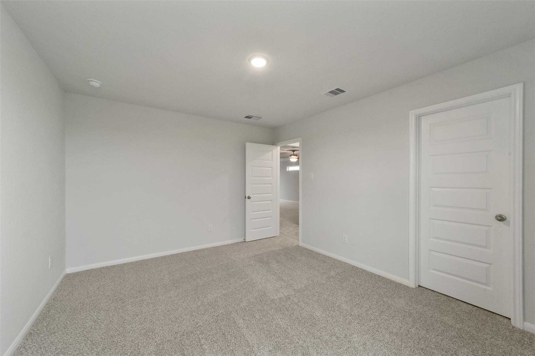 Spacious empty bedroom with neutral gray walls, beige carpet, and double doors in Davidson Homes The San Marcos E, Beasley, Texas