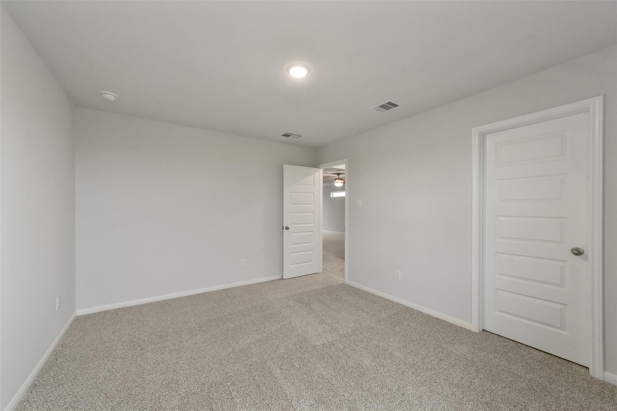 Empty bedroom with neutral gray walls, beige carpet, and double white doors in Davidson Homes The San Marcos E, Beasley, Texas