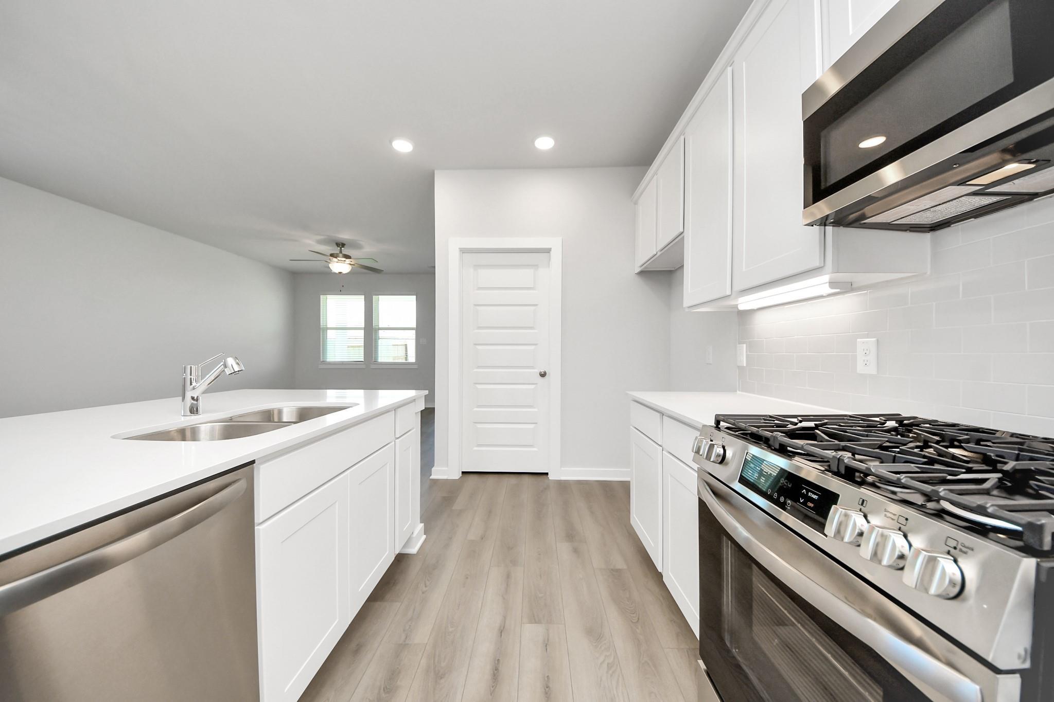 Modern kitchen with white cabinets, quartz countertops, and stainless appliances in The Costa A home at Emberly, Beasley, TX.