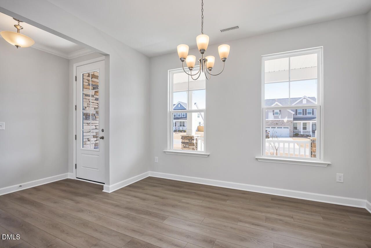 Bright dining room with elegant chandelier, large window viewing neighborhood homes, hardwood floors in The Willow G, Angier, NC
