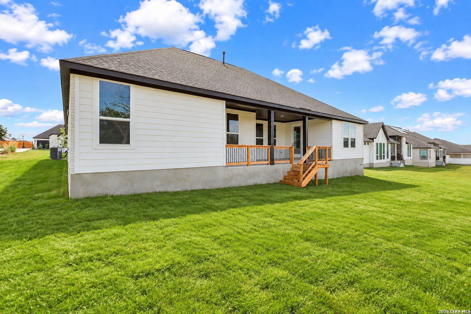 White one-story new construction home with covered patio and wooden stairs in spacious backyard at Potranco Oaks, Castroville, TX