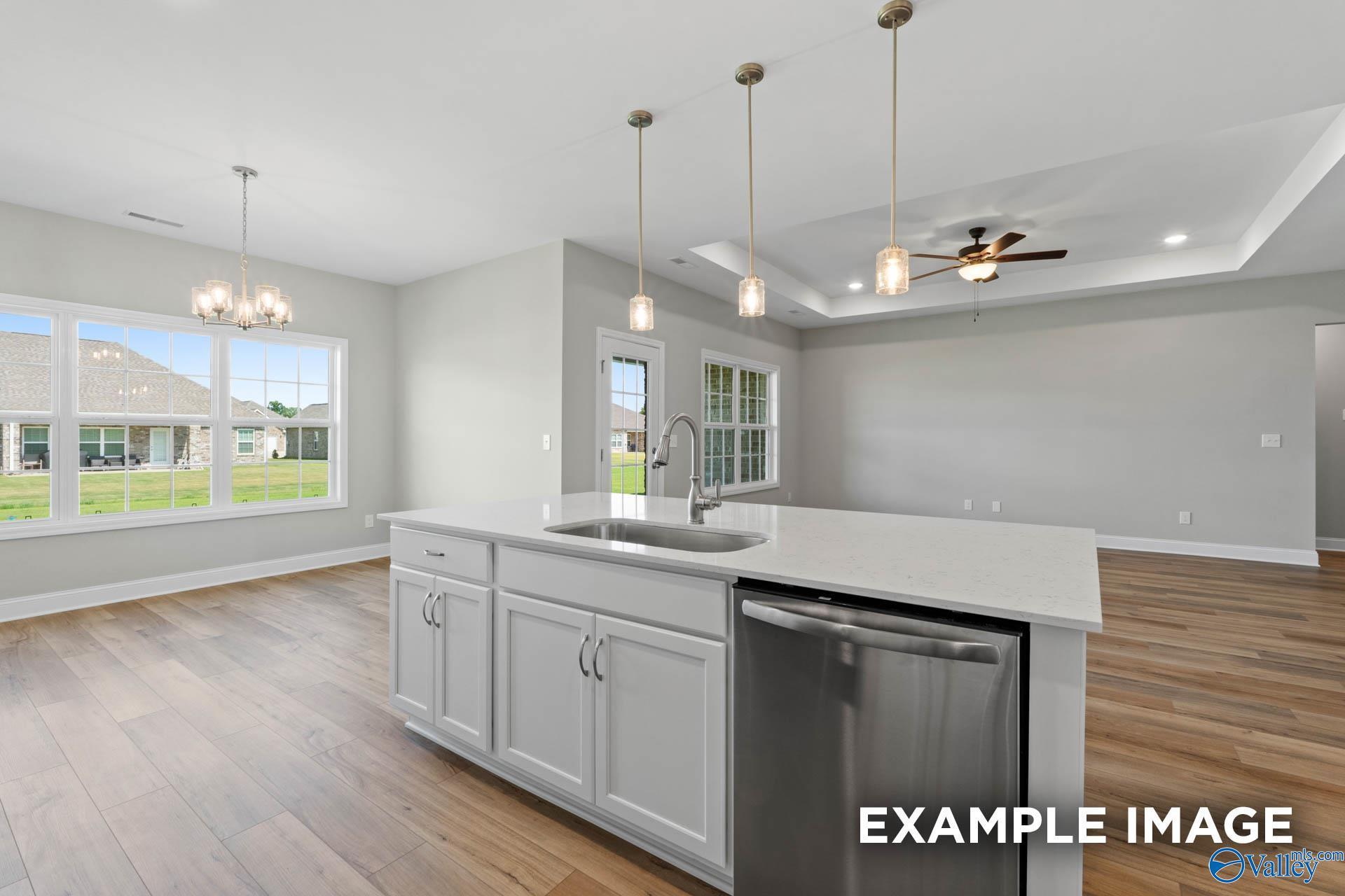 Modern open-concept kitchen with white island, stainless dishwasher, pendant lights, and backyard view in The Montgomery B, Hartselle, AL