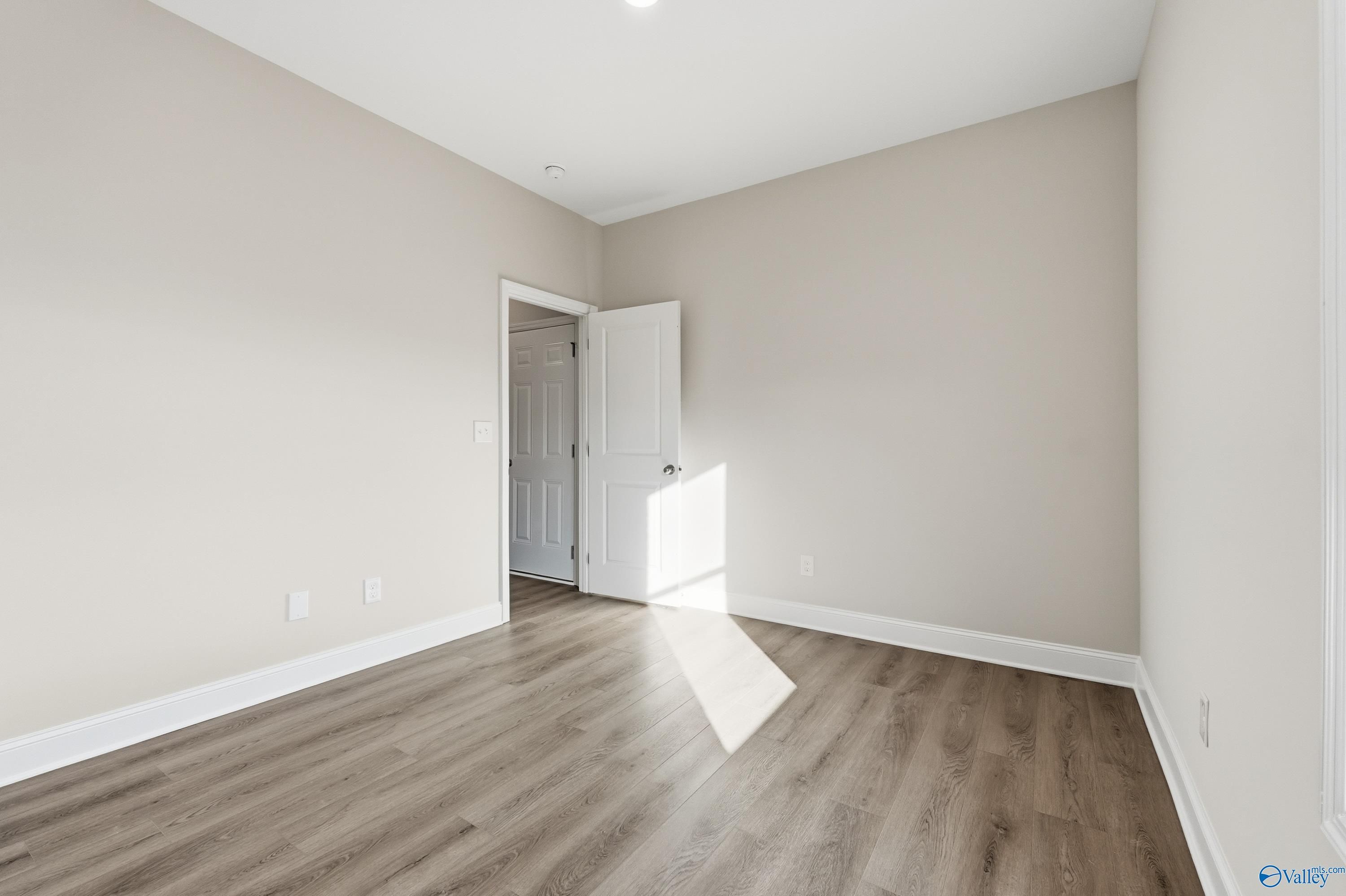 Sunlit secondary bedroom with beige walls, open white door, and hardwood floors in Davidson Homes The Daphne C, Arab, Alabama