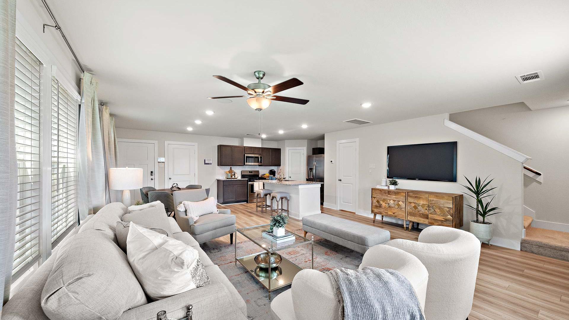 Open-concept living room and kitchen at Haven at Kieth Harrow in Cypress TX with gray sofas, wood floors, and ceiling fans