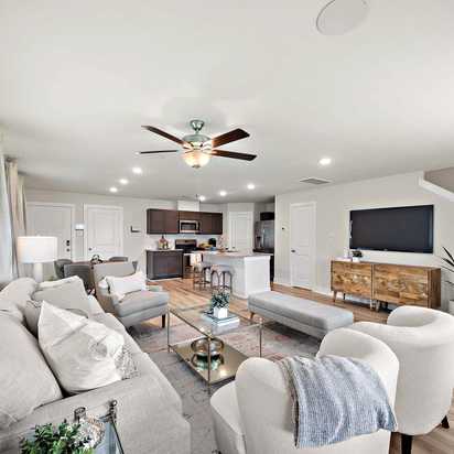 Open-concept living room and kitchen at Haven at Kieth Harrow in Cypress TX with gray sofas, wood floors, and ceiling fans