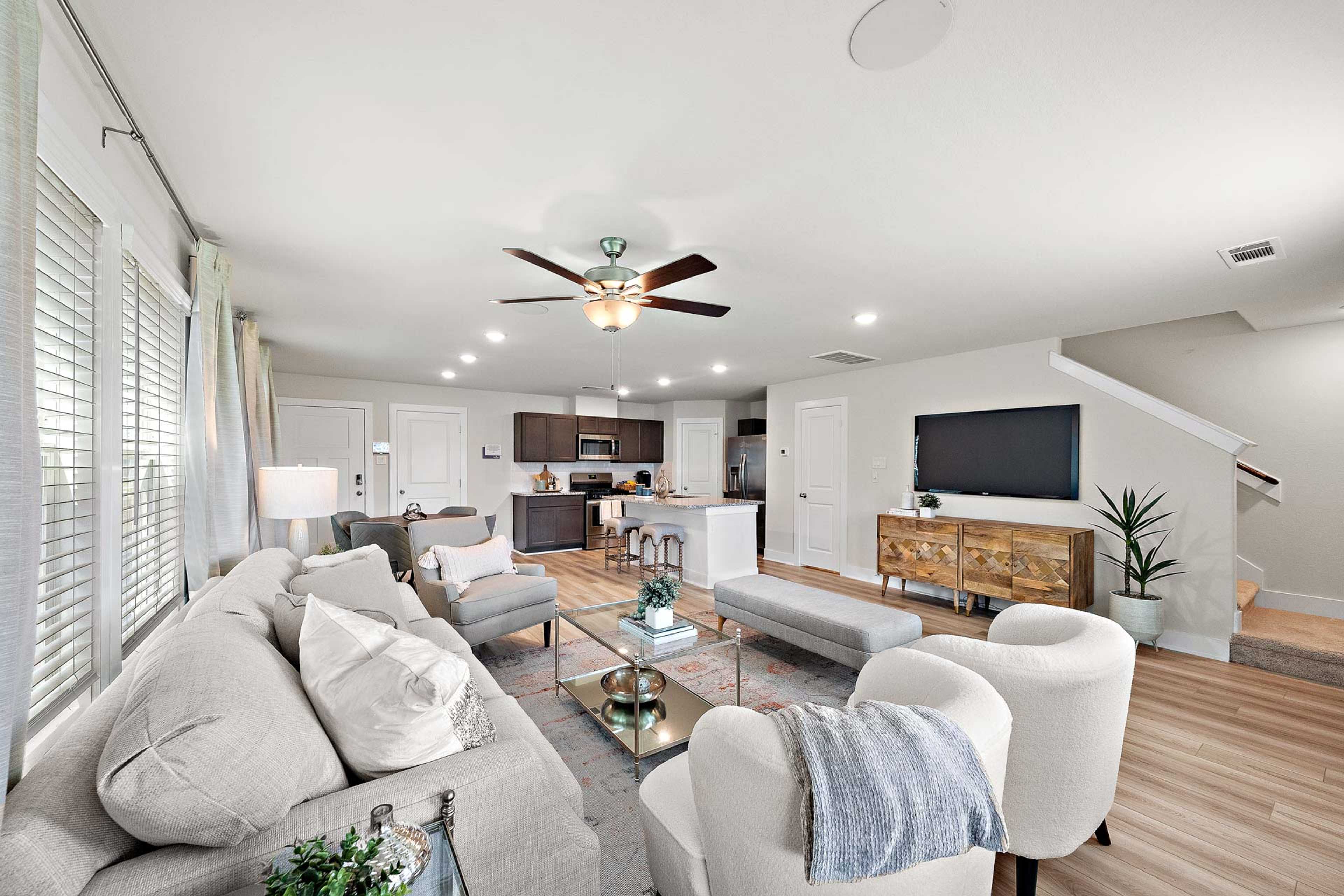 Open-concept living room and kitchen at Haven at Kieth Harrow in Cypress TX with gray sofa, ceiling fans, and hardwood floors