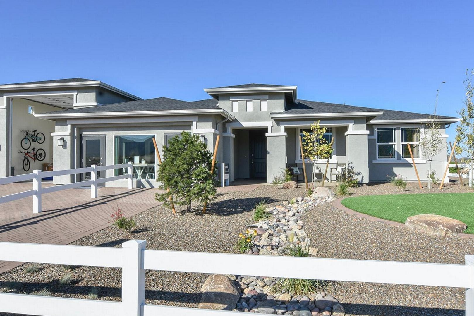 Modern single-story elevation of The Summit E home featuring gray siding, large windows, 3-car garage, white fence, and desert landscaping in Prescott Valley