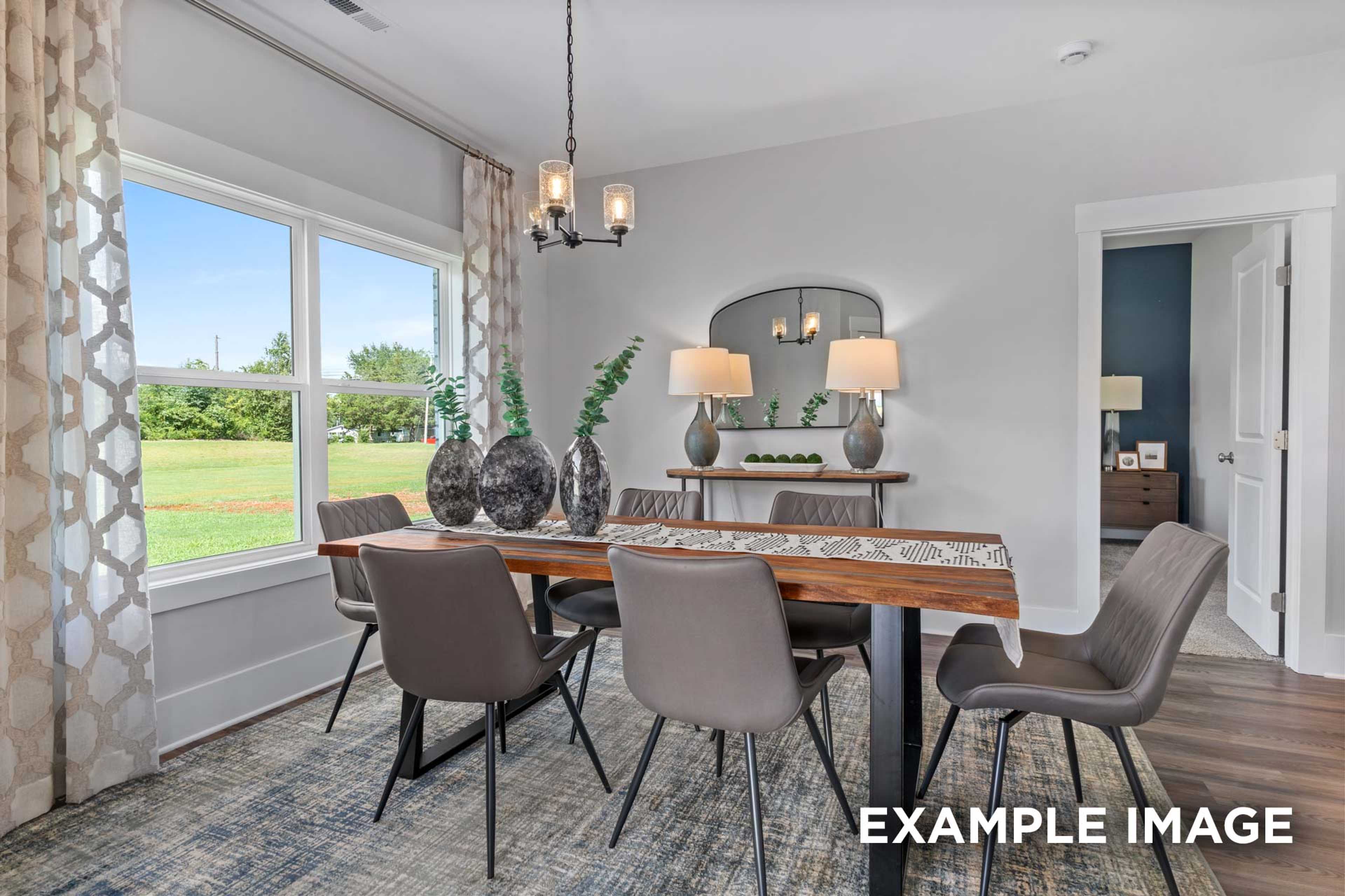 Spacious dining room in The Franklin C with wooden table, upholstered chairs, chandelier, and large windows overlooking green fields