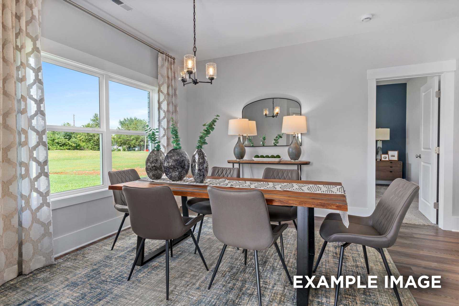 Spacious dining room in The Franklin C with wooden table, upholstered chairs, chandelier, and large windows overlooking green fields
