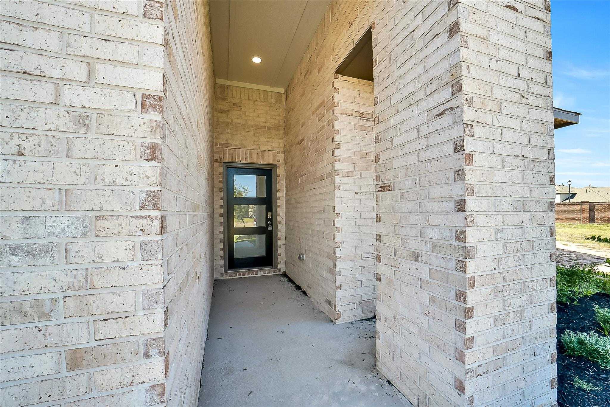 Brick front entryway with covered porch, modern black glass door, and landscaping in Davidson Homes The Acadia A, Sunterra, Katy, Texas