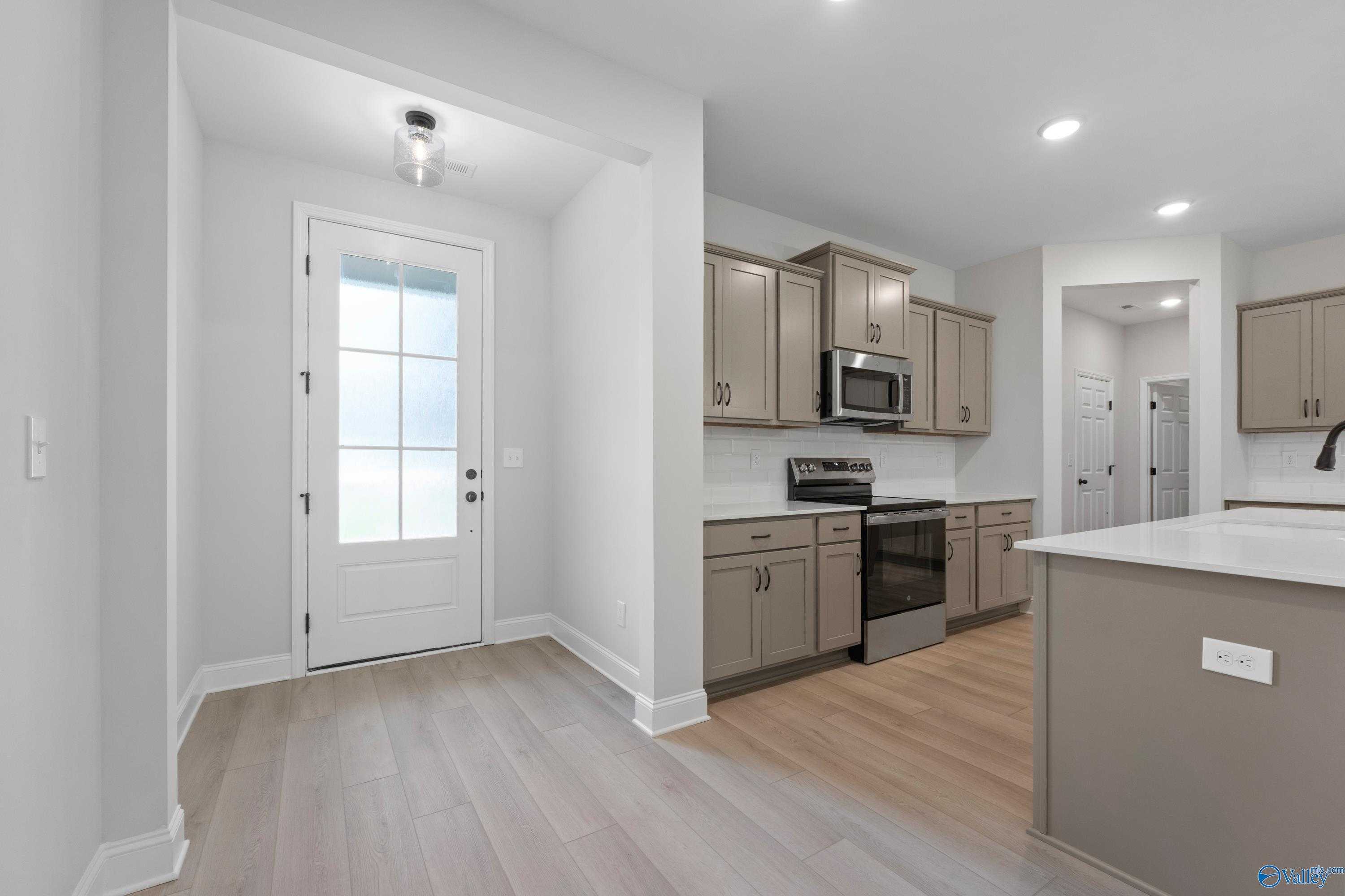 Open kitchen featuring stainless steel appliances, beige cabinets, and large island next to glass-paneled back door in Davidson Homes The Kirkland, Harvest, AL