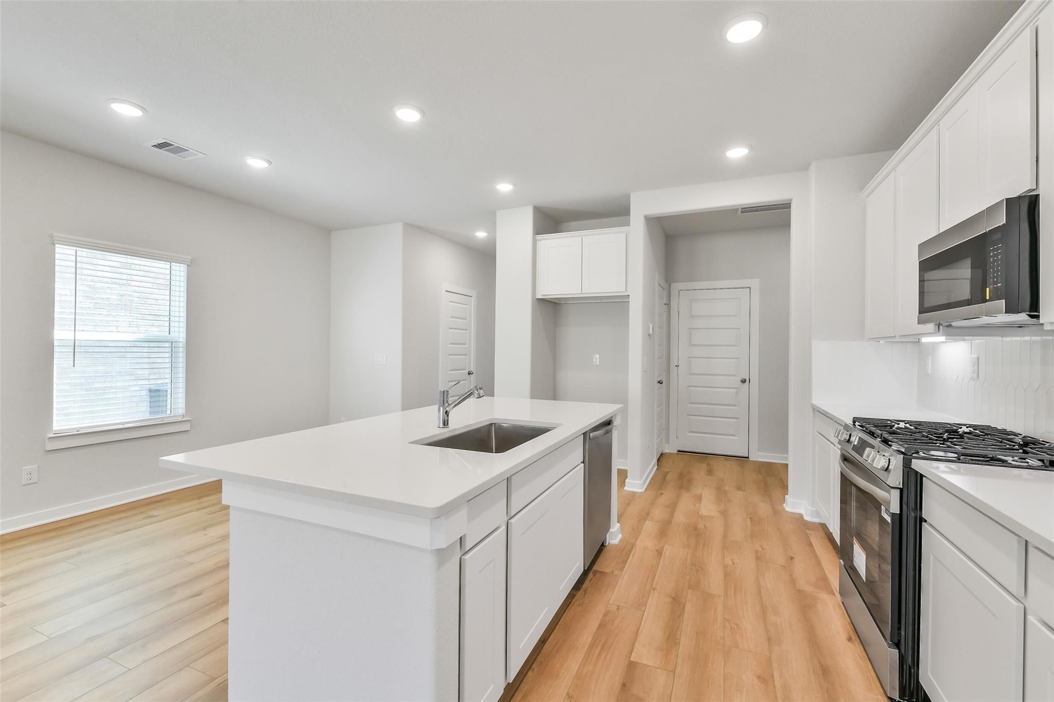 Modern white kitchen with large island sink, stainless steel appliances, hardwood floors in The Blanco E floor plan, Magnolia, Texas