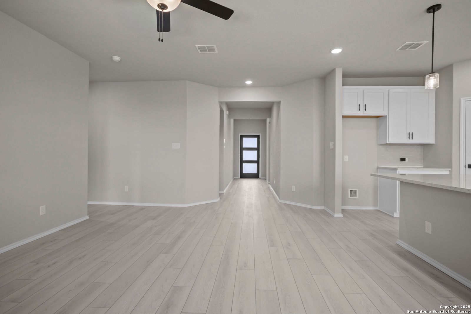 Spacious entry hallway with ceiling fan and gray laminate floors leading to white cabinet kitchen in Davidson Homes Asheville E, Converse TX
