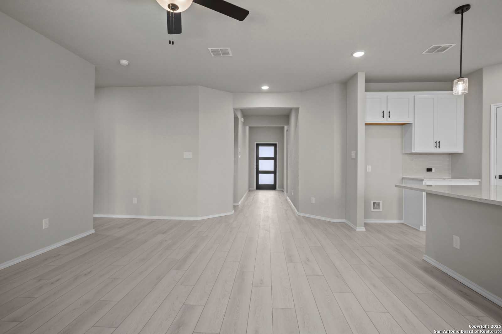 Spacious entry hallway with ceiling fan and gray laminate floors leading to white cabinet kitchen in Davidson Homes Asheville E, Converse TX