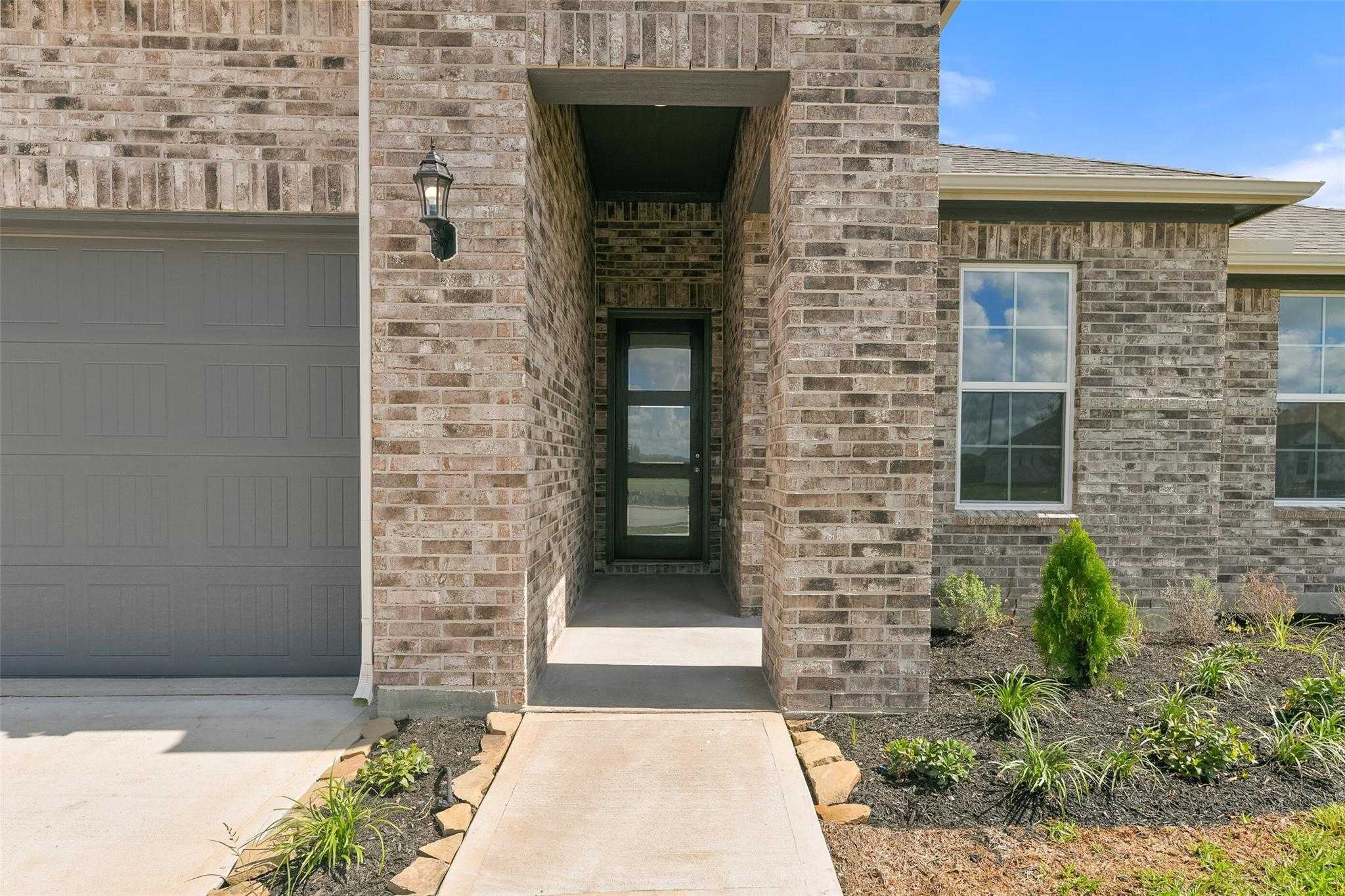 Brick facade with 2-car garage, glass front door, lantern light, and landscaped entry in Davidson Homes The Edward A, Lago Mar, Texas City