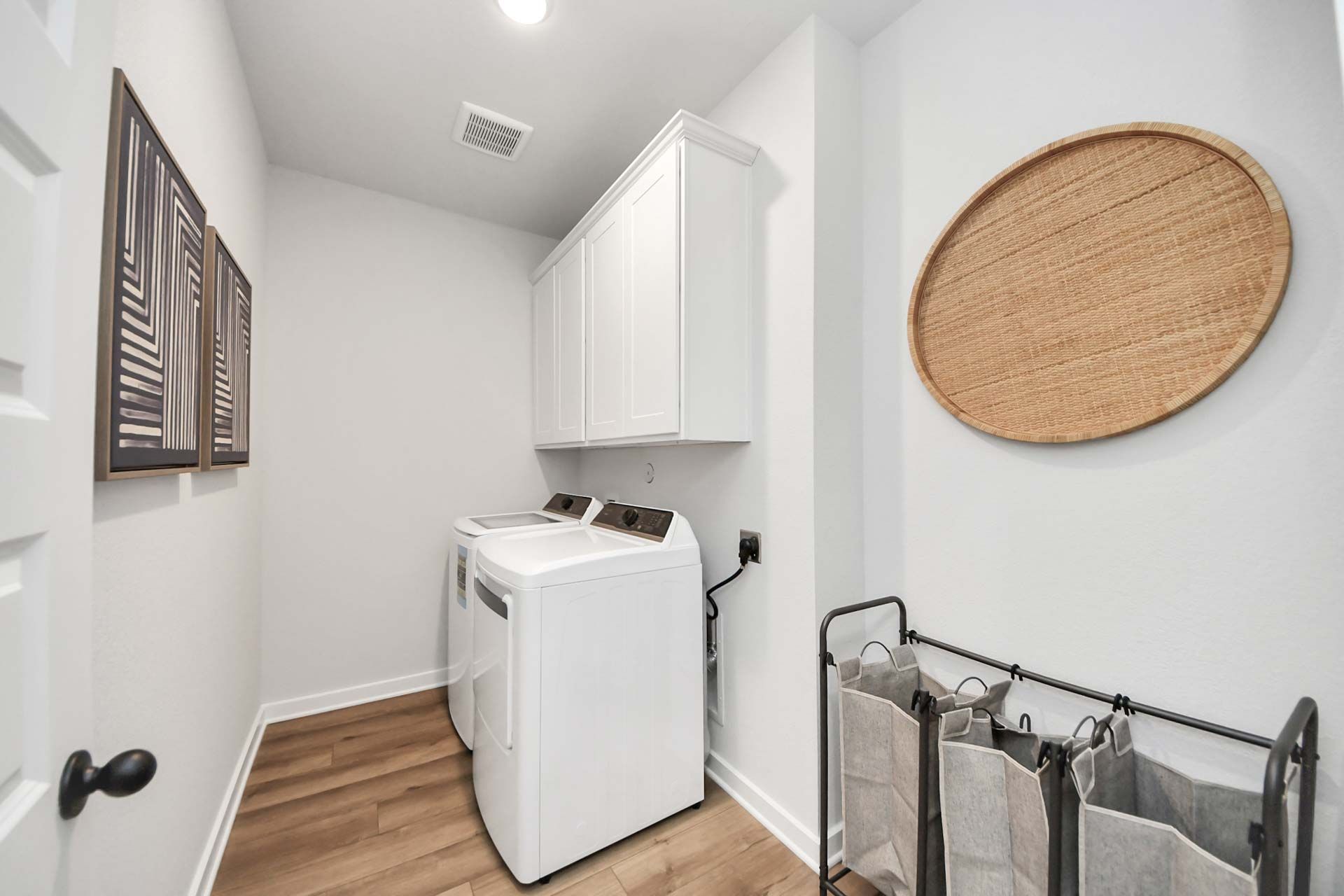 Laundry room at Enclave at Newport in Crosby, TX featuring white cabinets, modern washer and dryer, and wood-look flooring.