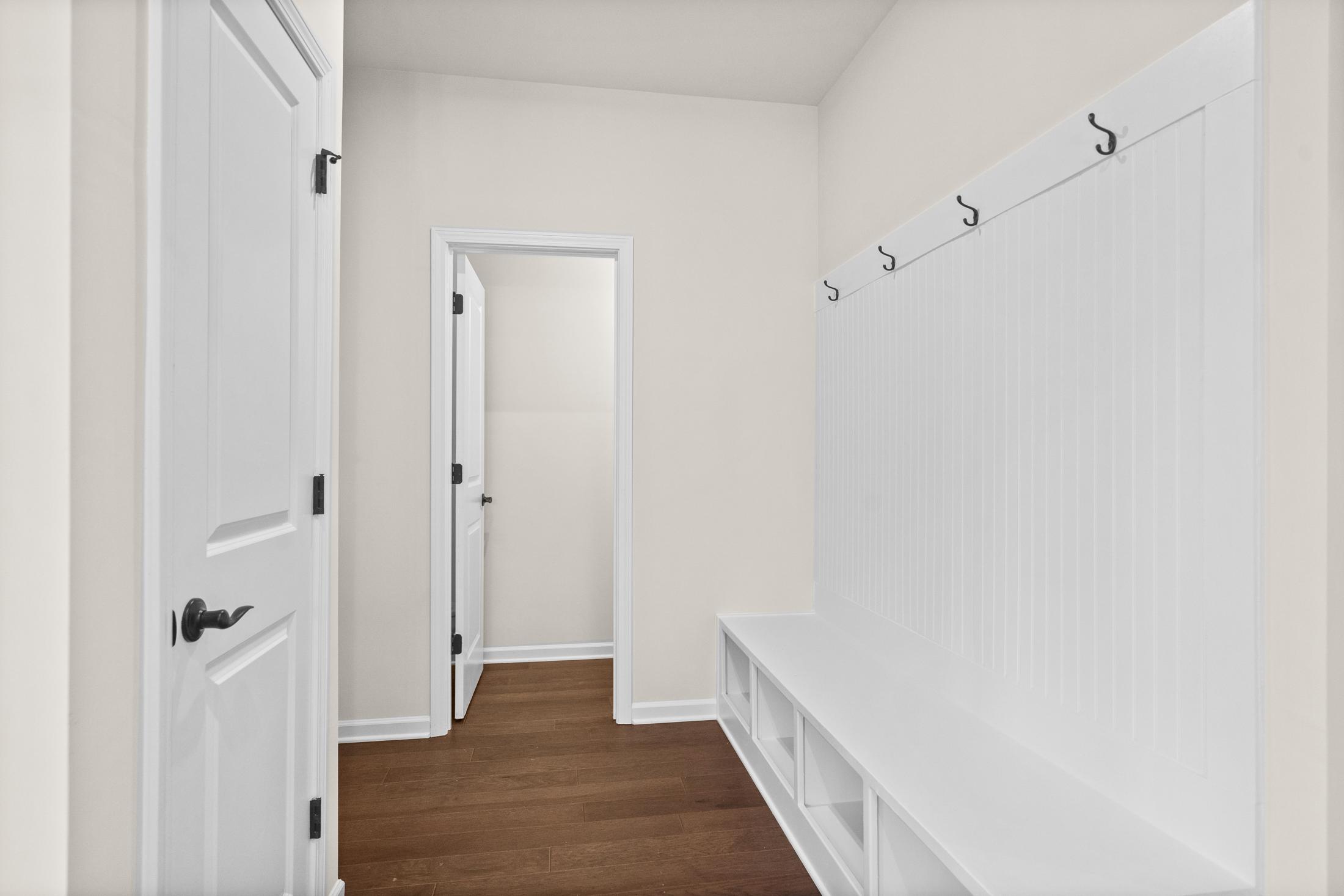 Spacious mudroom in The Glenwood home design with built-in white bench, storage cubbies, coat hooks, hardwood floors