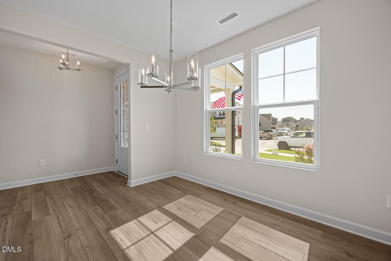 Bright dining area with luxury vinyl plank floors, modern chandelier, and large windows in Davidson Homes The Willow C, Zebulon, NC
